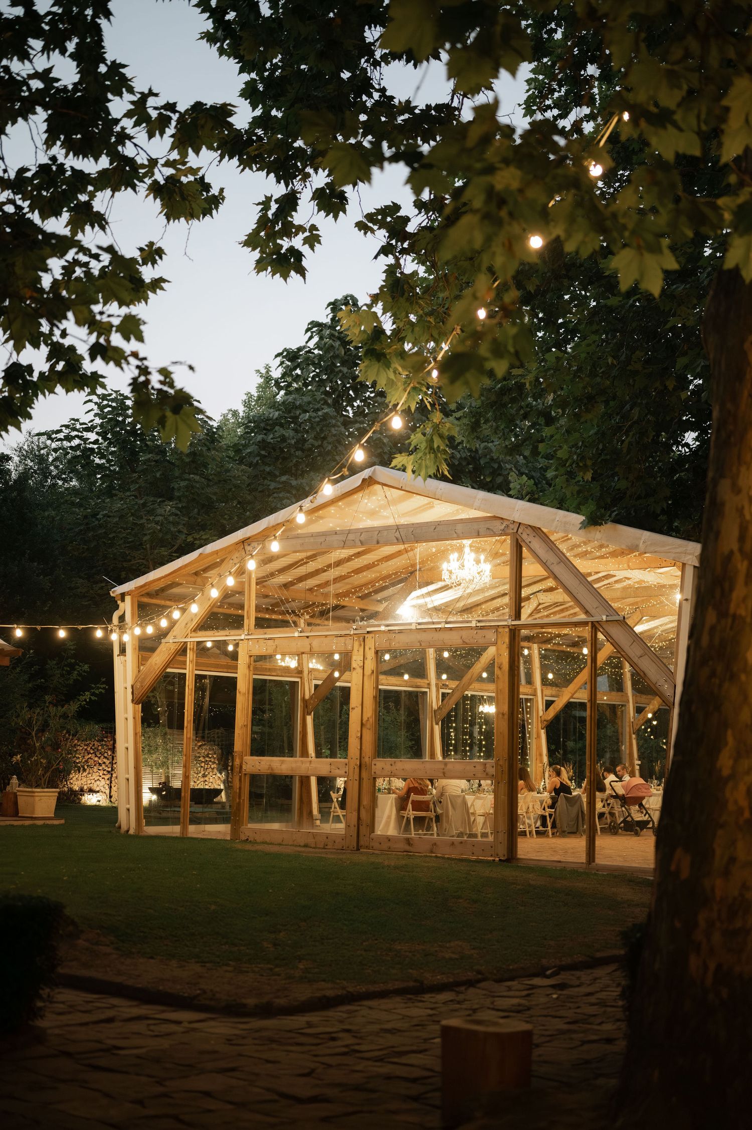 A rustic outdoor wedding venue with string lights illuminating a wooden barn-style structure at dusk.