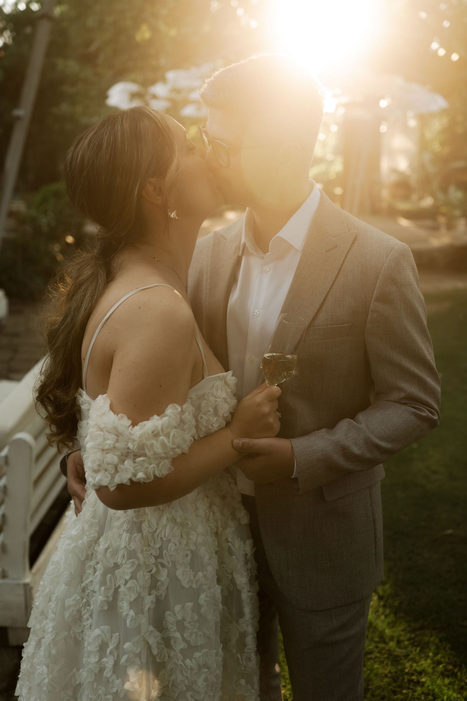A couple shares an intimate moment at sunset in a garden setting, with the bride wearing a flowing white gown.