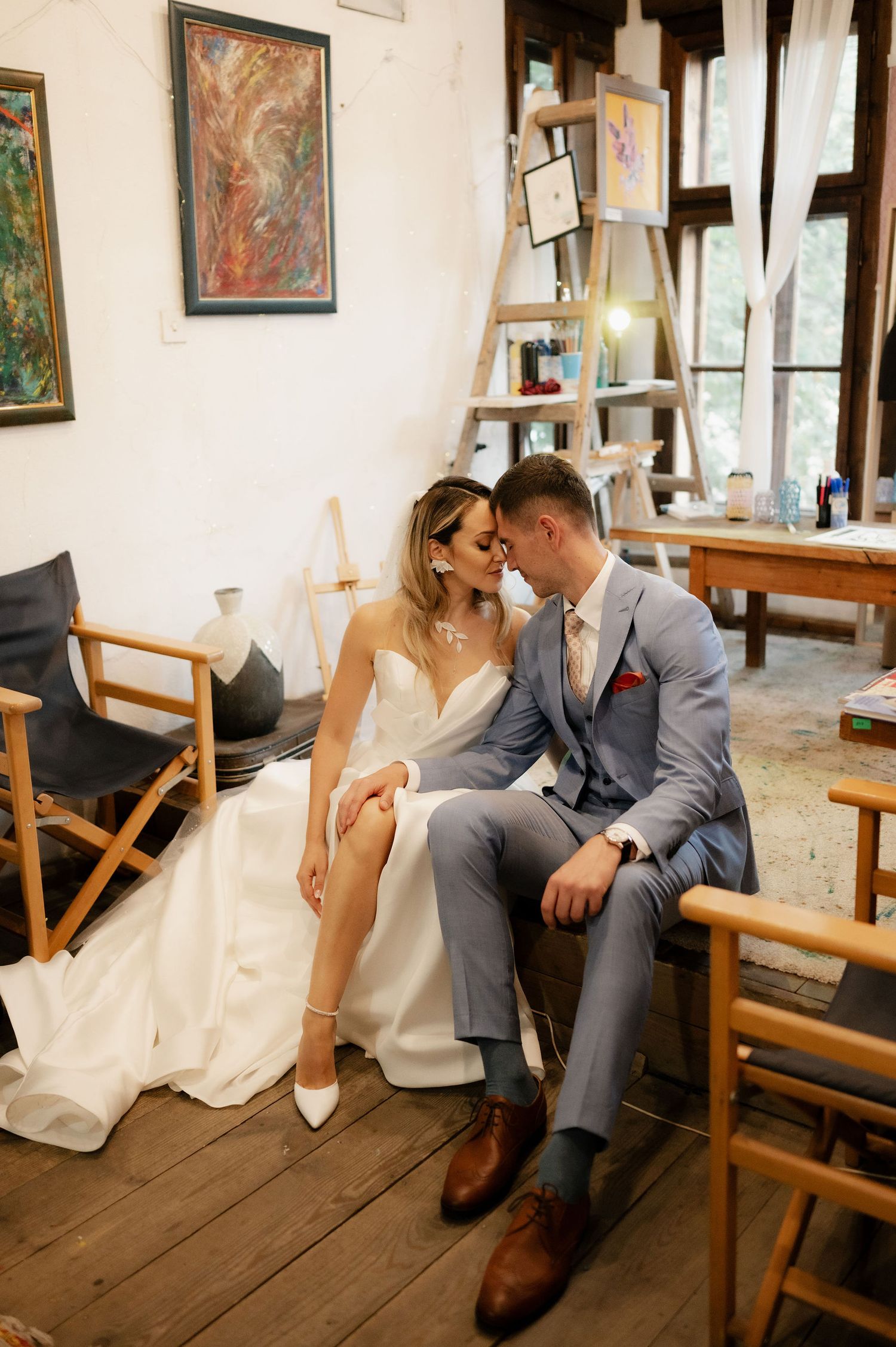 A romantic wedding couple shares intimate moments on wooden benches in a rustic indoor setting.