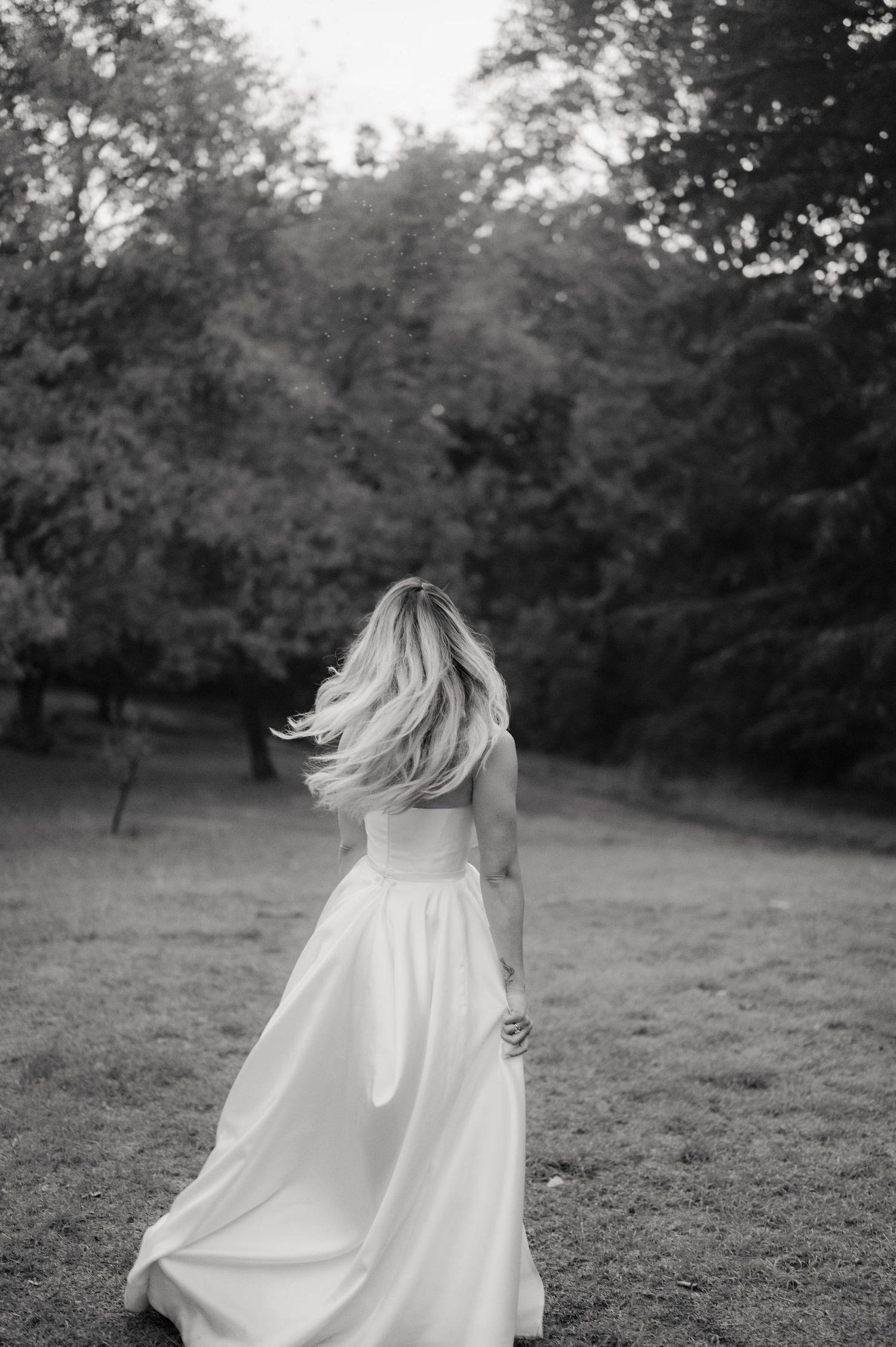 A flowing white dress twirls gracefully in a black and white photograph taken in a serene outdoor setting.