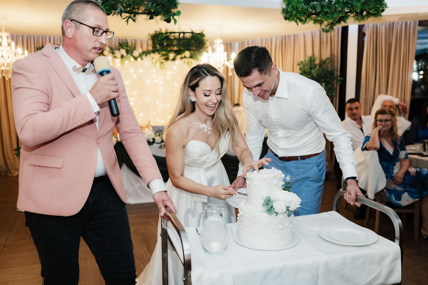 Wedding couple cuts their elegant white tiered cake together at their reception celebration.