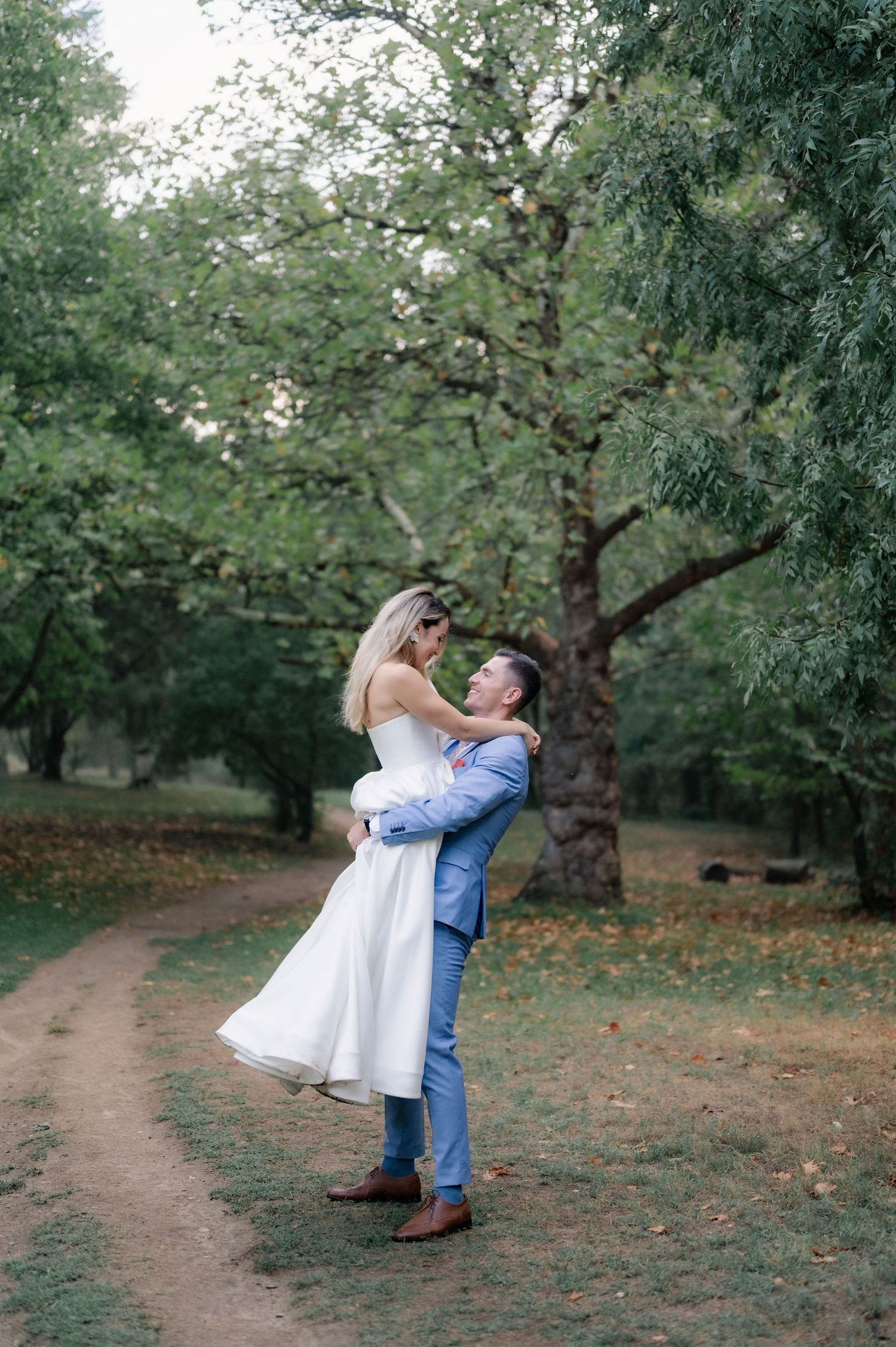 A romantic wedding moment captured in an orchard as a couple embraces on a rustic dirt path.