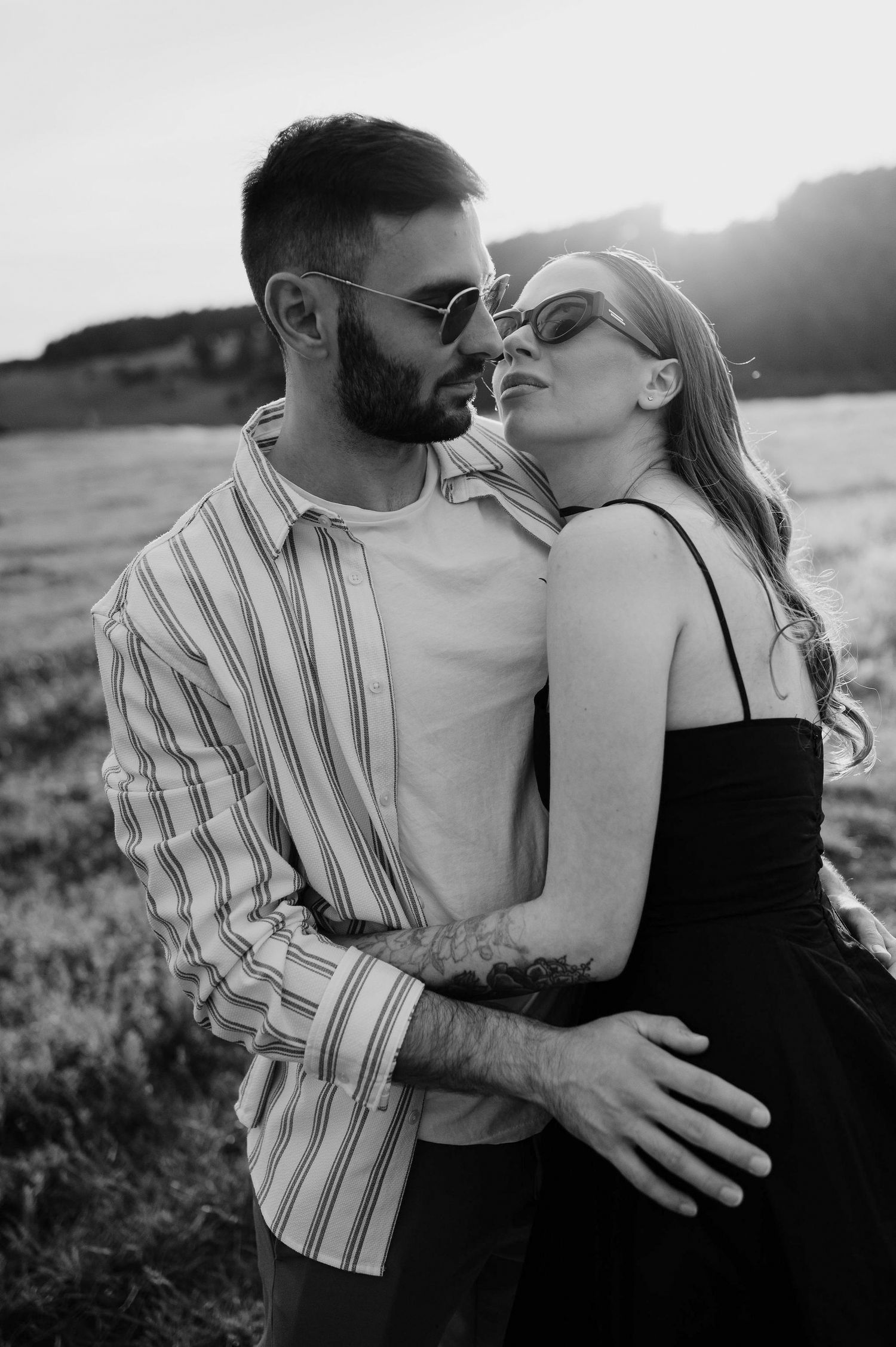 A romantic black and white photo series showing a couple embracing and kissing in a field at sunset.