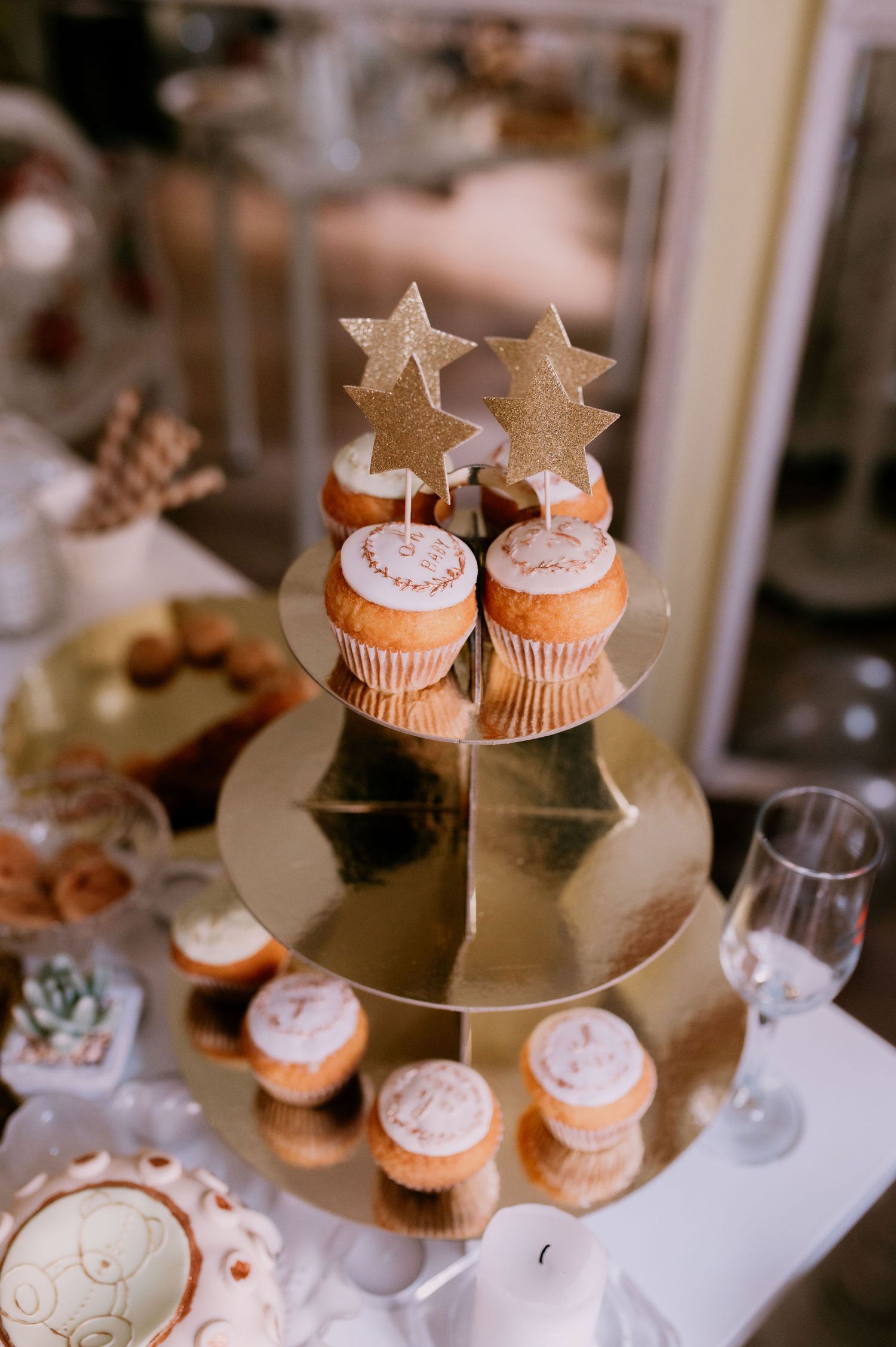 Elegant cupcakes topped with frosting and gold star decorations displayed on a tiered white dessert stand at a party.