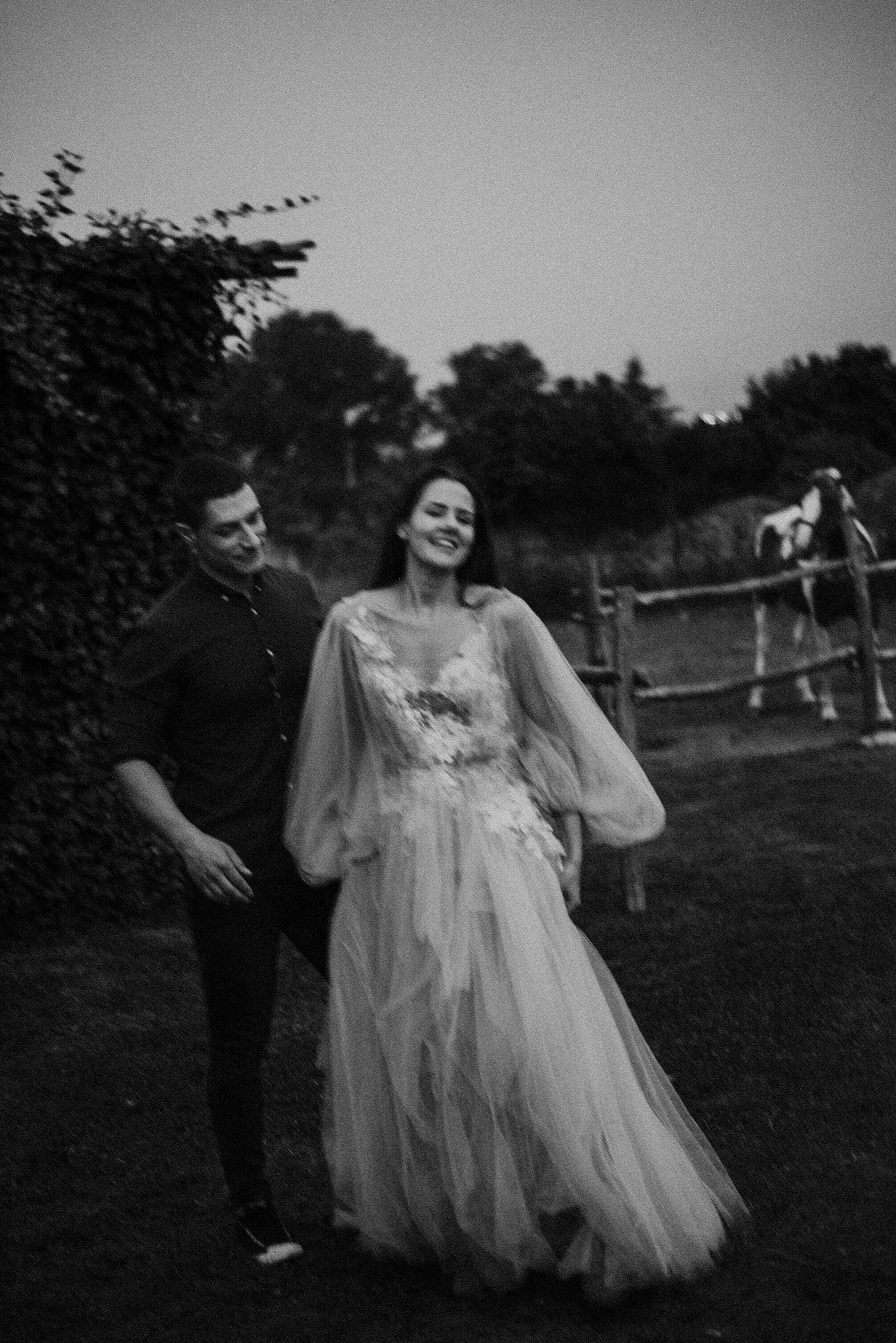 A couple laughing together outdoors in a garden setting with a rustic fence in the background.