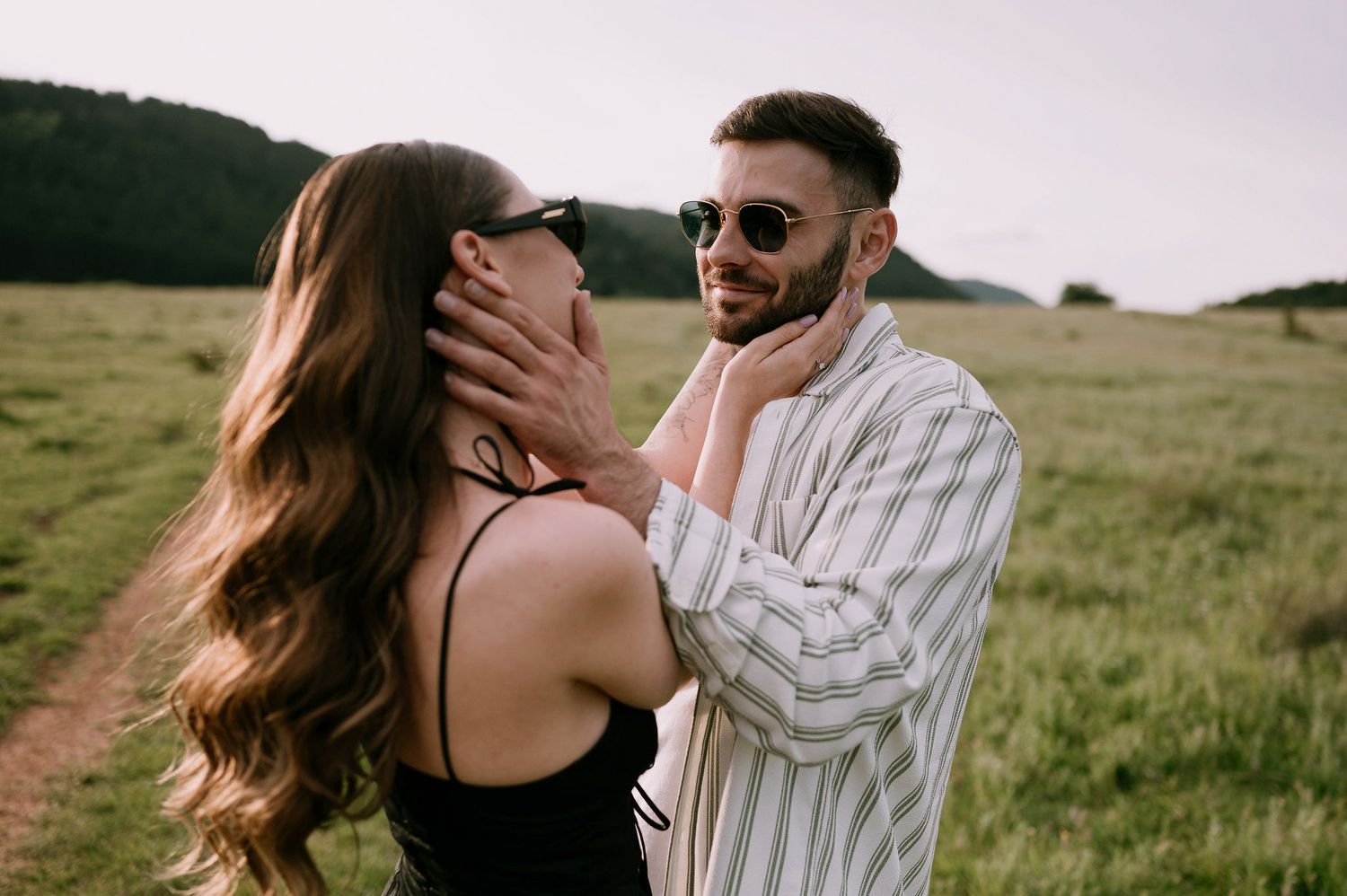 A couple shares intimate moments in a grassy field during a golden hour photoshoot.