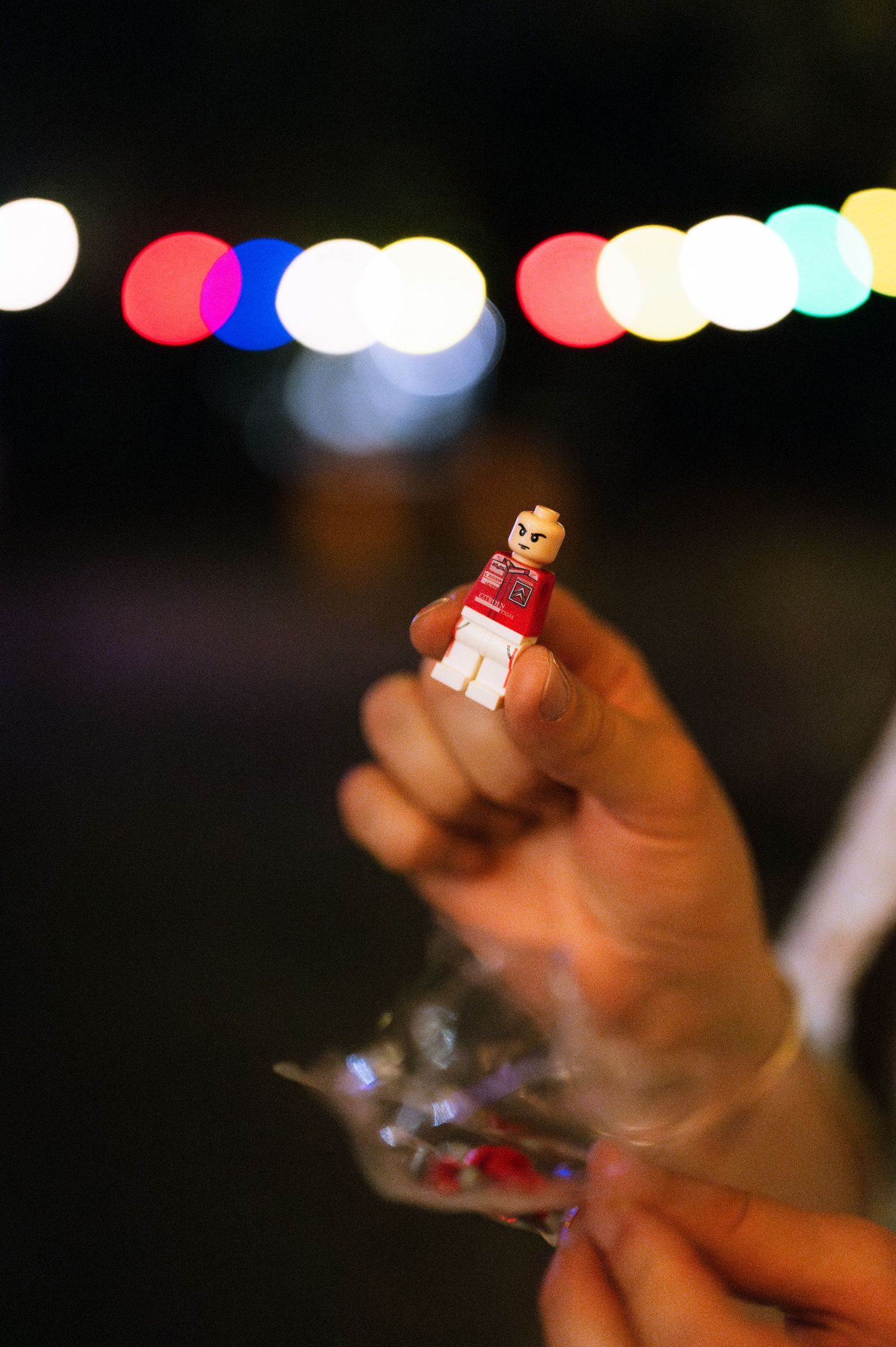 A small toy figure held up against a blurred background of colorful bokeh lights.