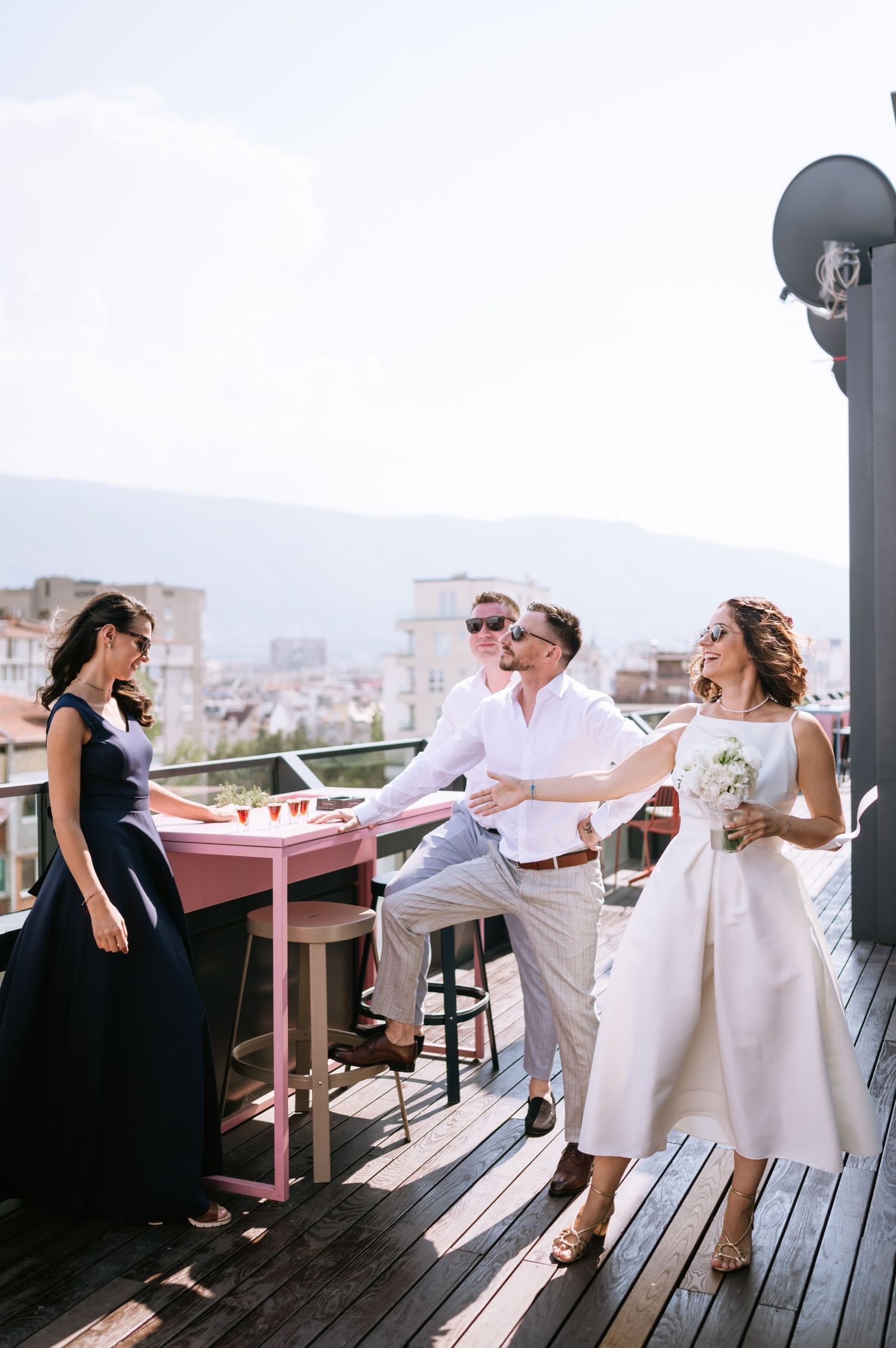 A couple dances together on a wooden deck terrace overlooking a city view during a celebration.
