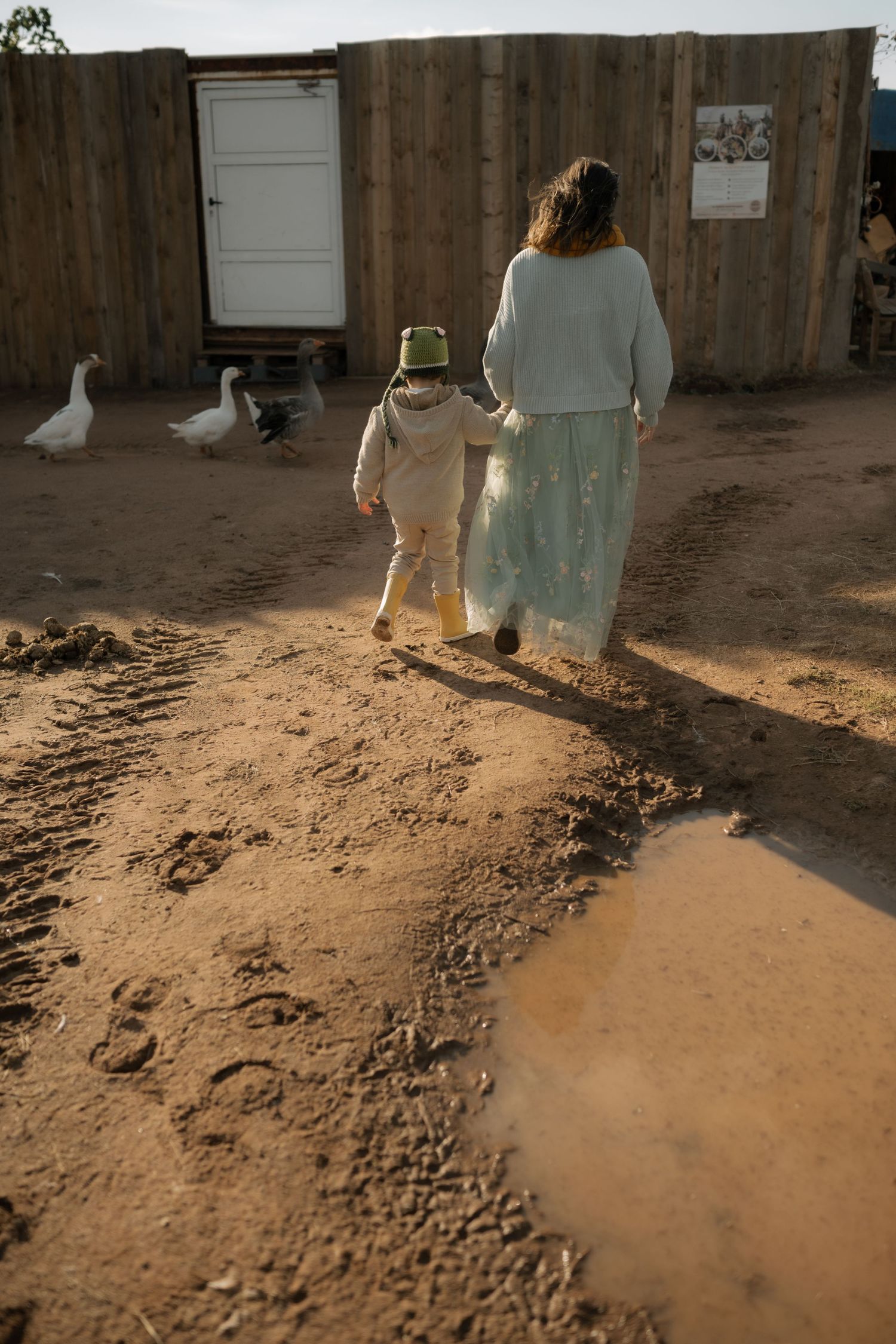 Two figures walk along a dusty dirt path at sunset casting long shadows in warm golden light.