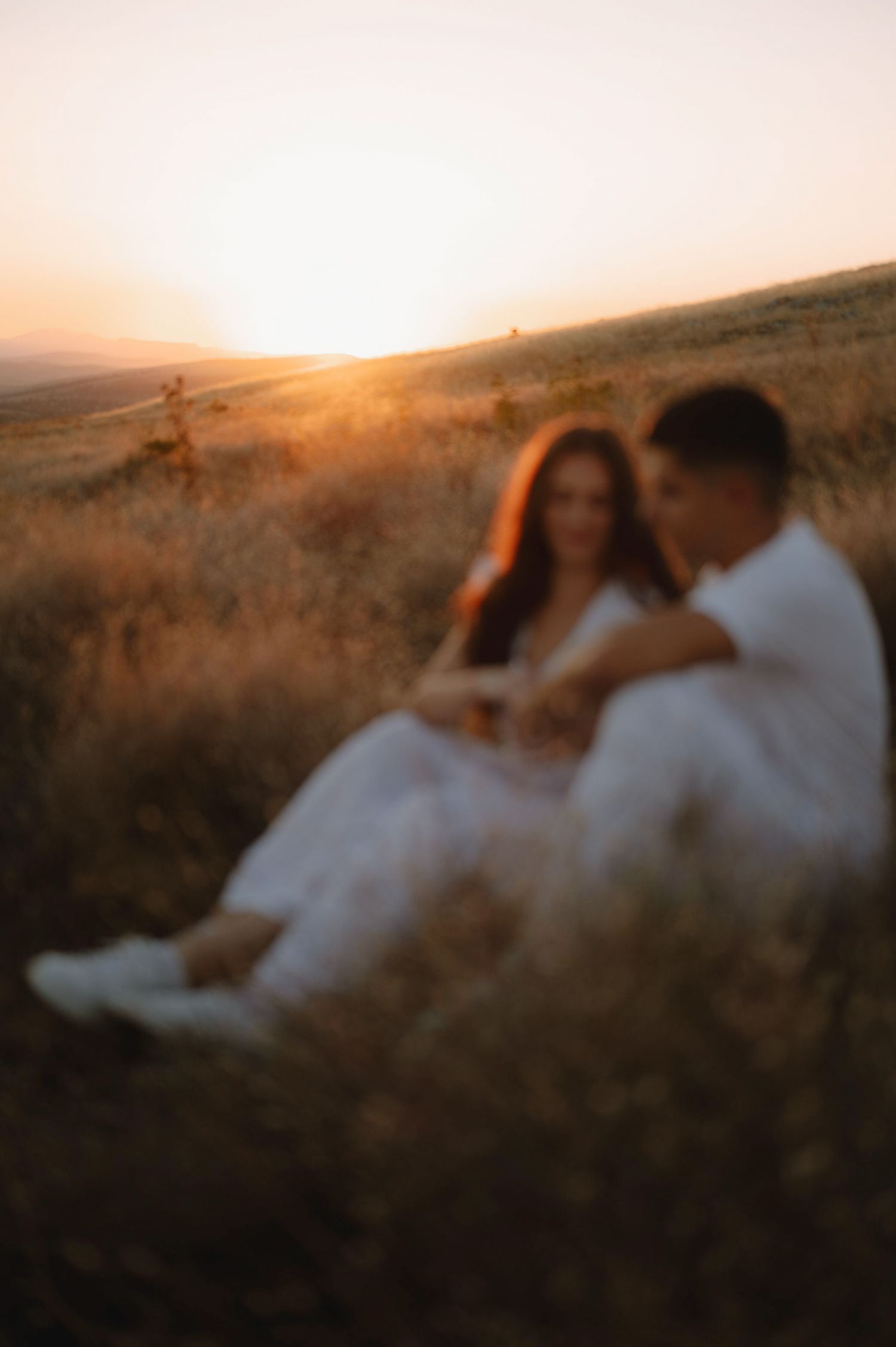 A couple embraces in a romantic sunset moment on a hilltop with golden light illuminating the scene.