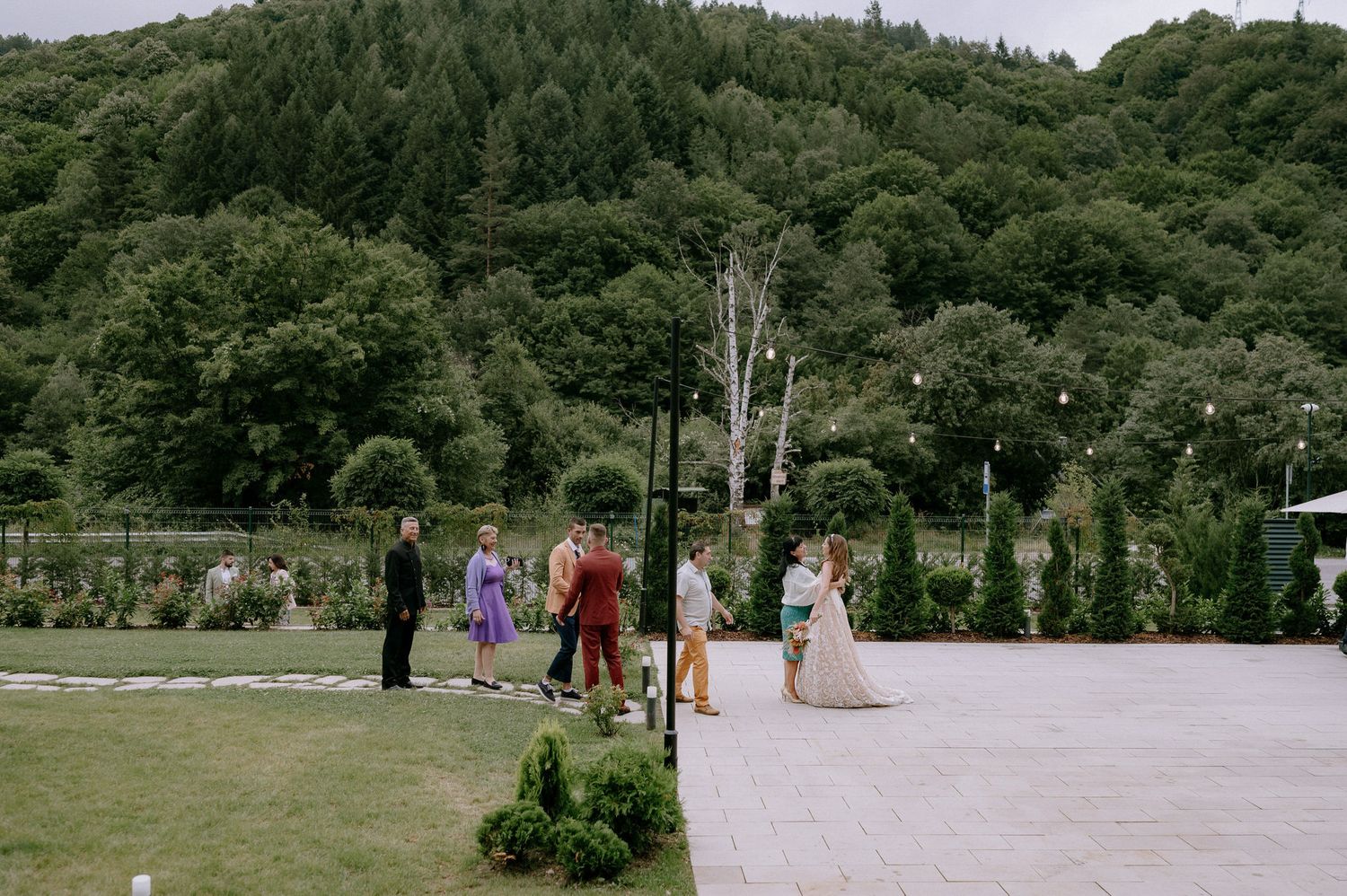 Guests gather outdoors for a scenic wedding ceremony surrounded by lush green forest and mountains.
