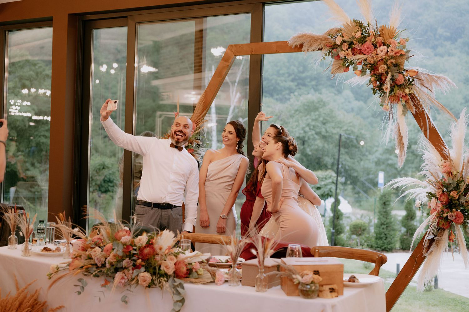 A wedding celebration in a glass-walled venue overlooking mountains with floral decorations and table settings.
