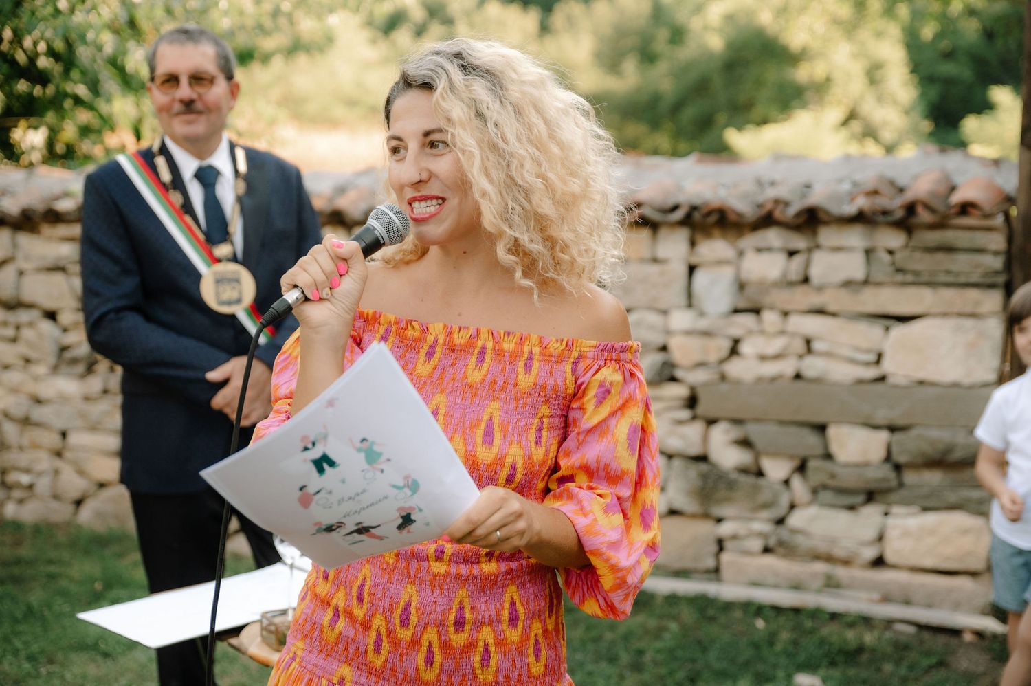 A couple shares a joyful moment during an outdoor ceremony with a stone wall backdrop in natural lighting.