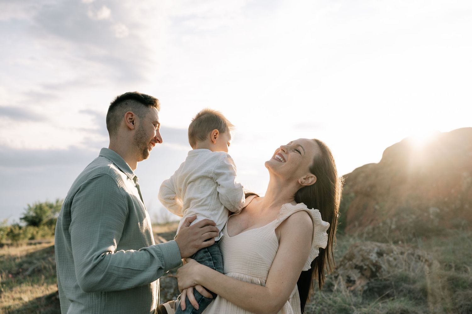 A couple embraces in a sunlit field during golden hour, creating a romantic silhouette against the warm sky.