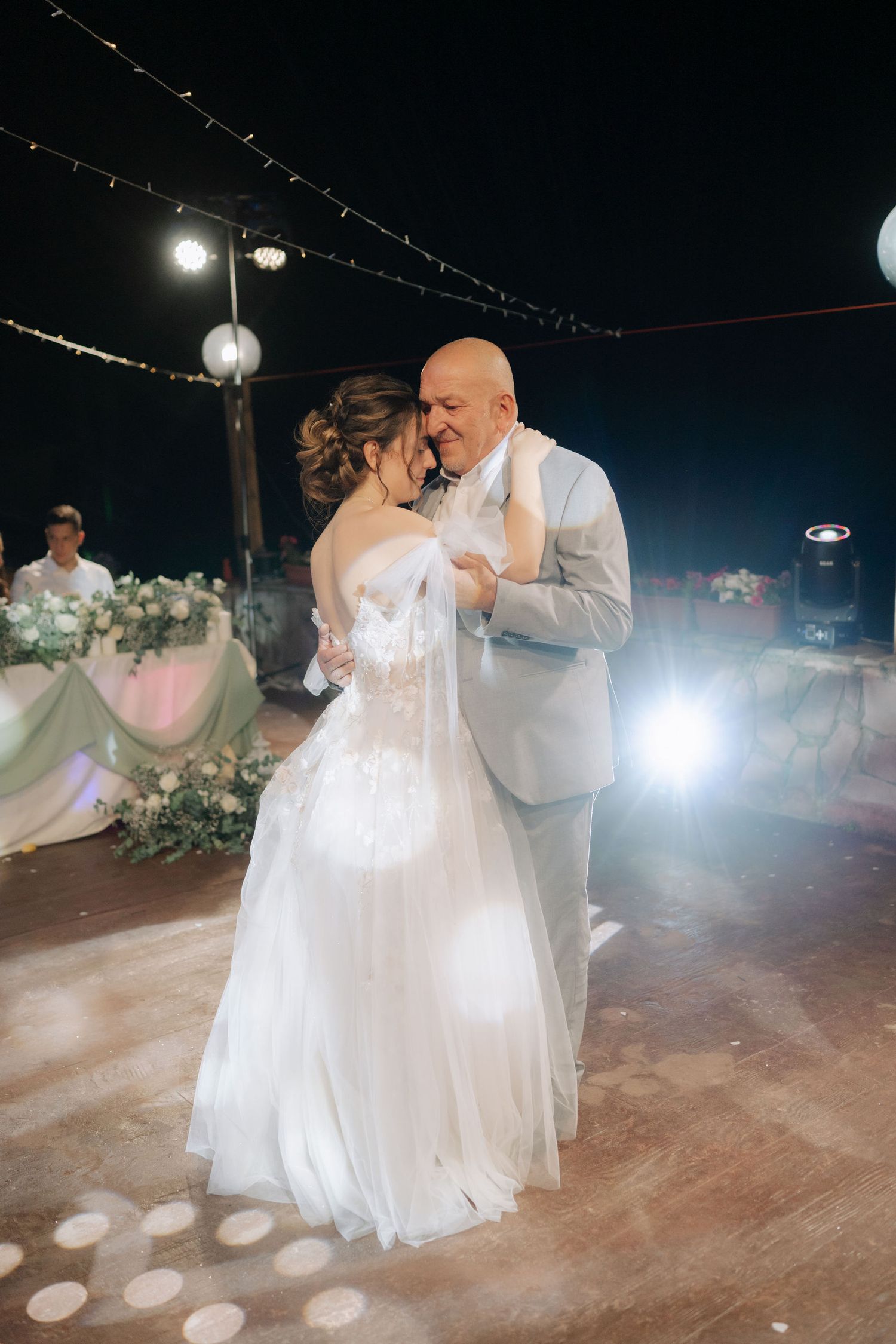 A couple shares their first dance as newlyweds on an outdoor dance floor under twinkling lights at night.