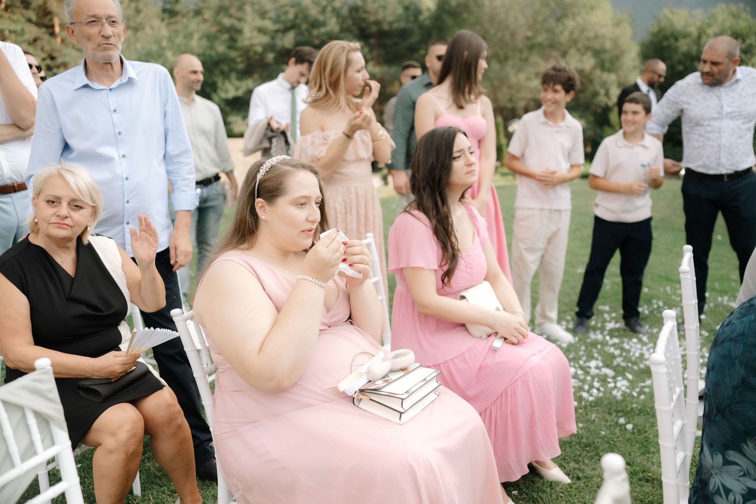 Wedding guests gather outdoors on a sunny day wearing pink and neutral colored attire.