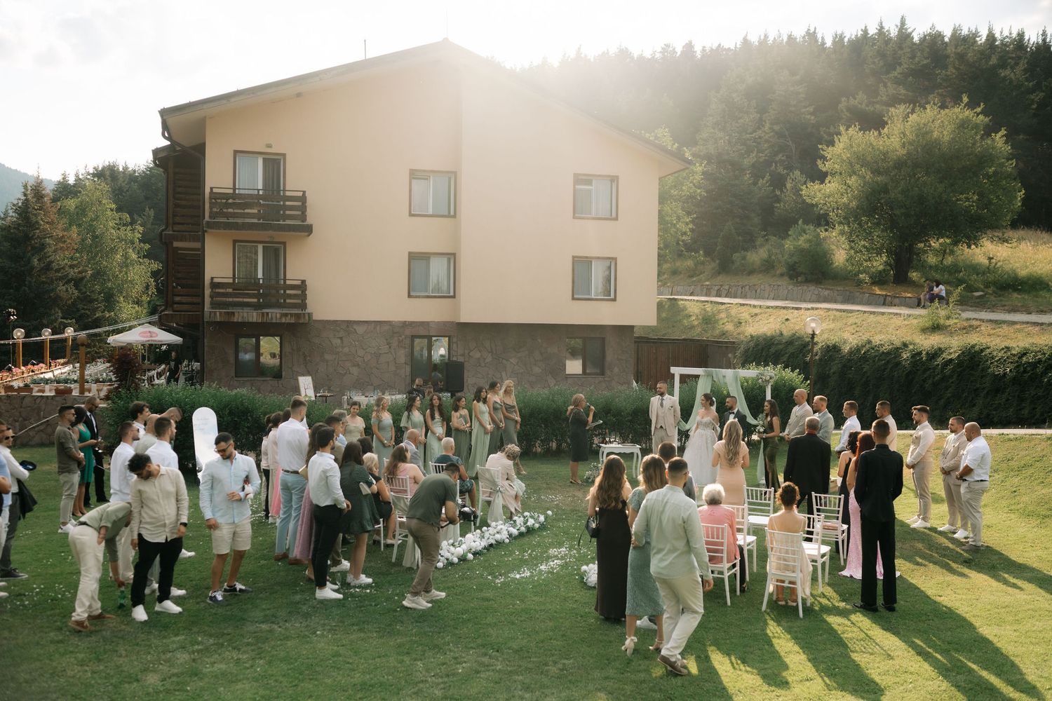Outdoor wedding reception gathering on a sunny lawn with guests mingling in front of a modern apartment building.