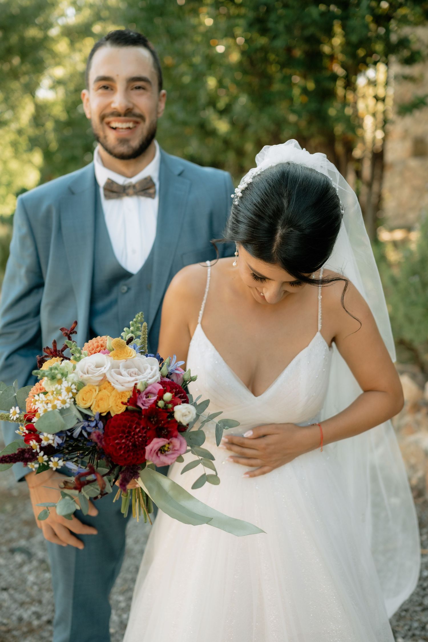 Romantic wedding couple embraces outdoors with vibrant fall bouquet featuring burgundy and orange flowers.