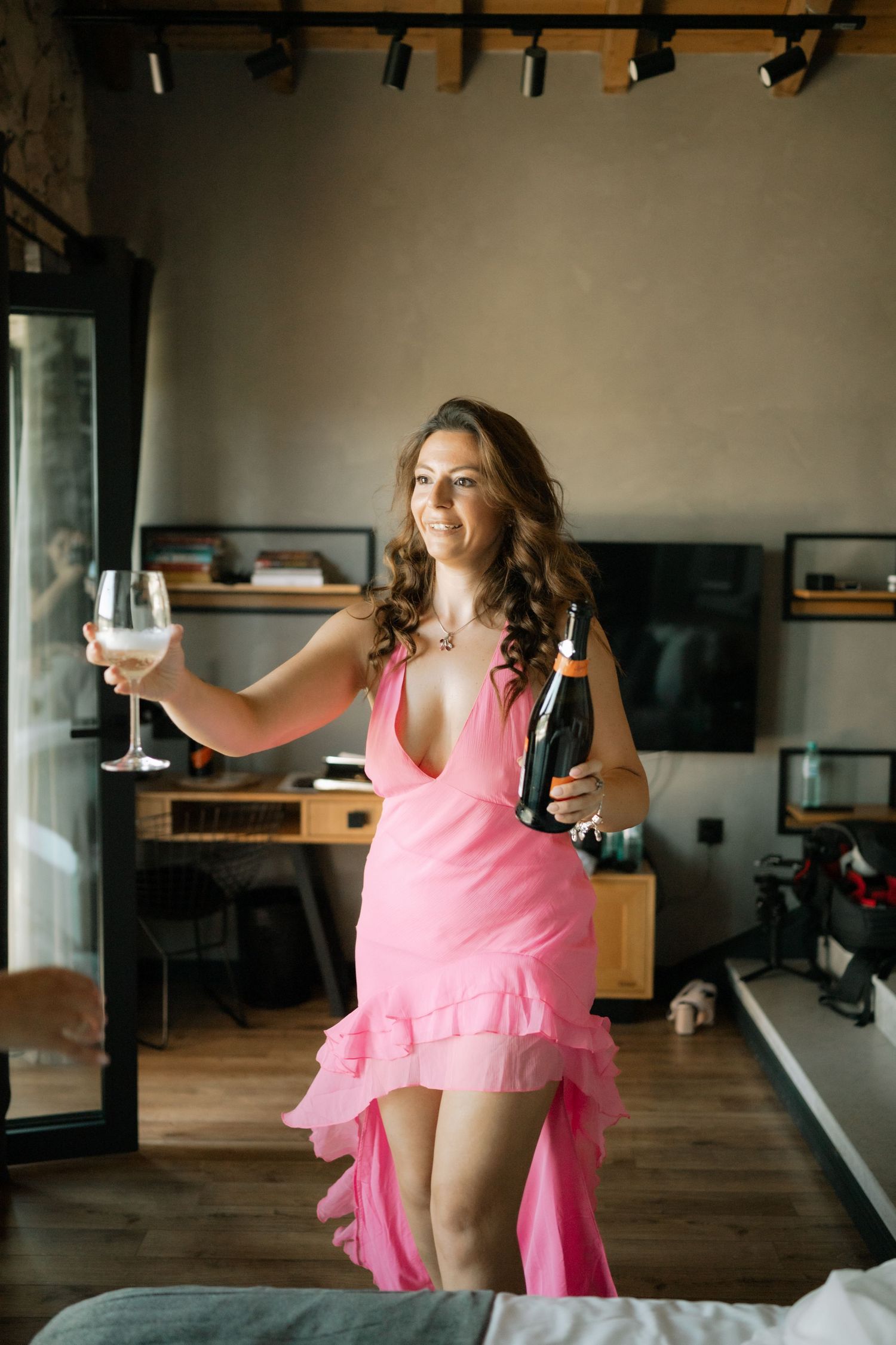 A dancer in a flowing pink dress performs graceful movements in a sunlit dance studio with wooden floors.