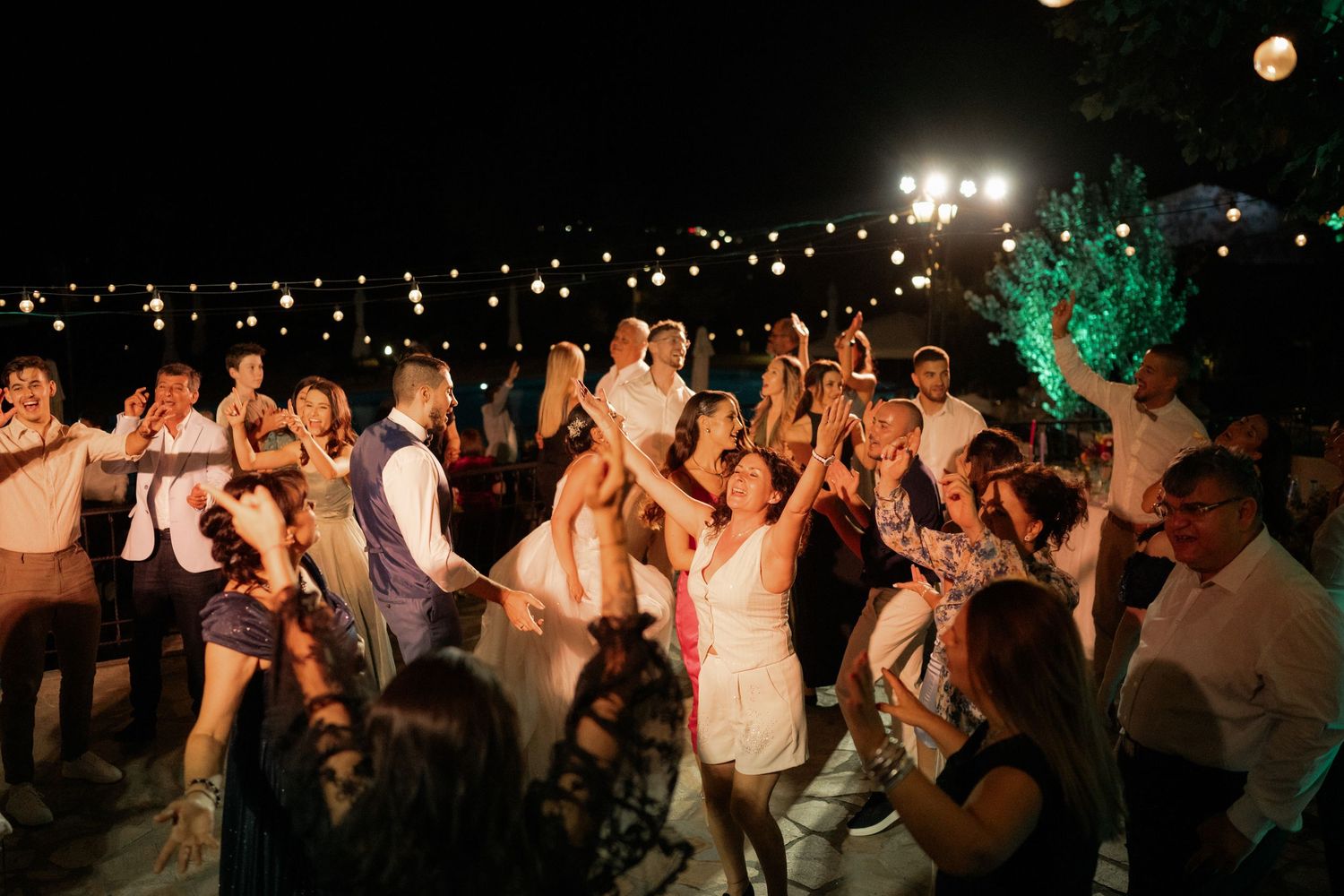 A crowd of wedding guests dancing and celebrating at a lively nighttime outdoor reception.