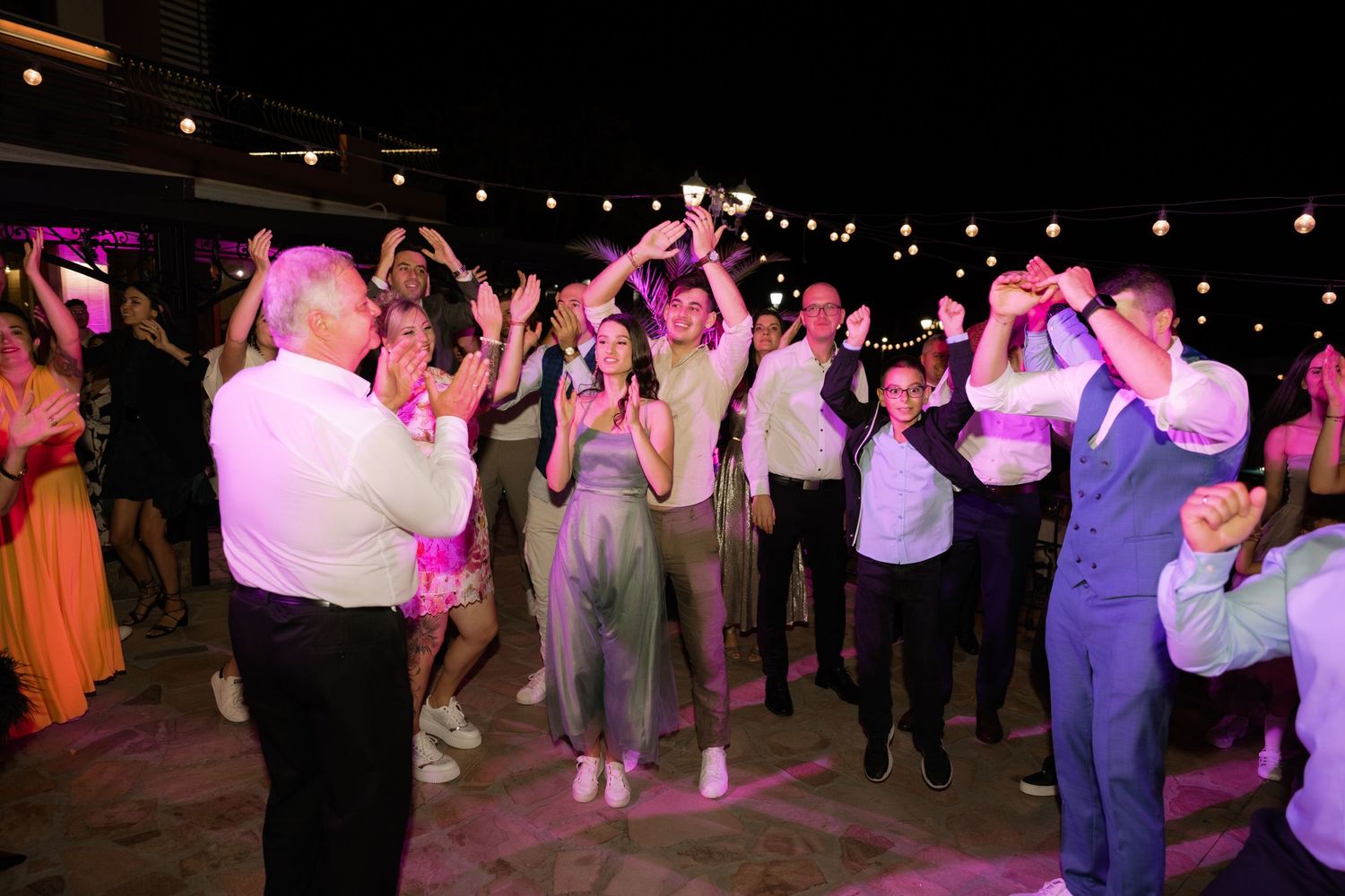 A festive dance party scene with pink and purple lighting where guests dance beneath twinkling string lights.