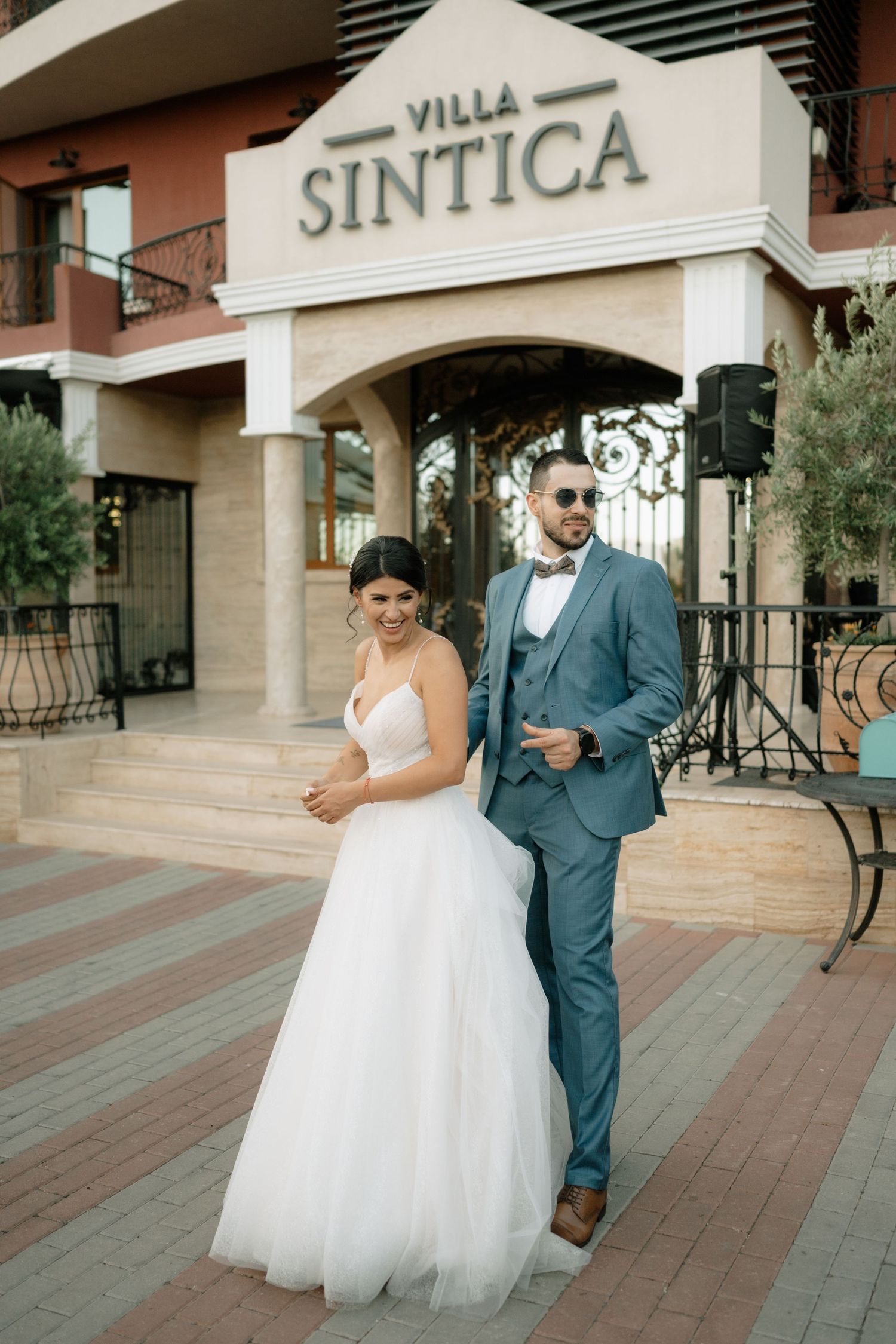A couple in wedding attire shares a joyful moment together walking outside a Villa building.