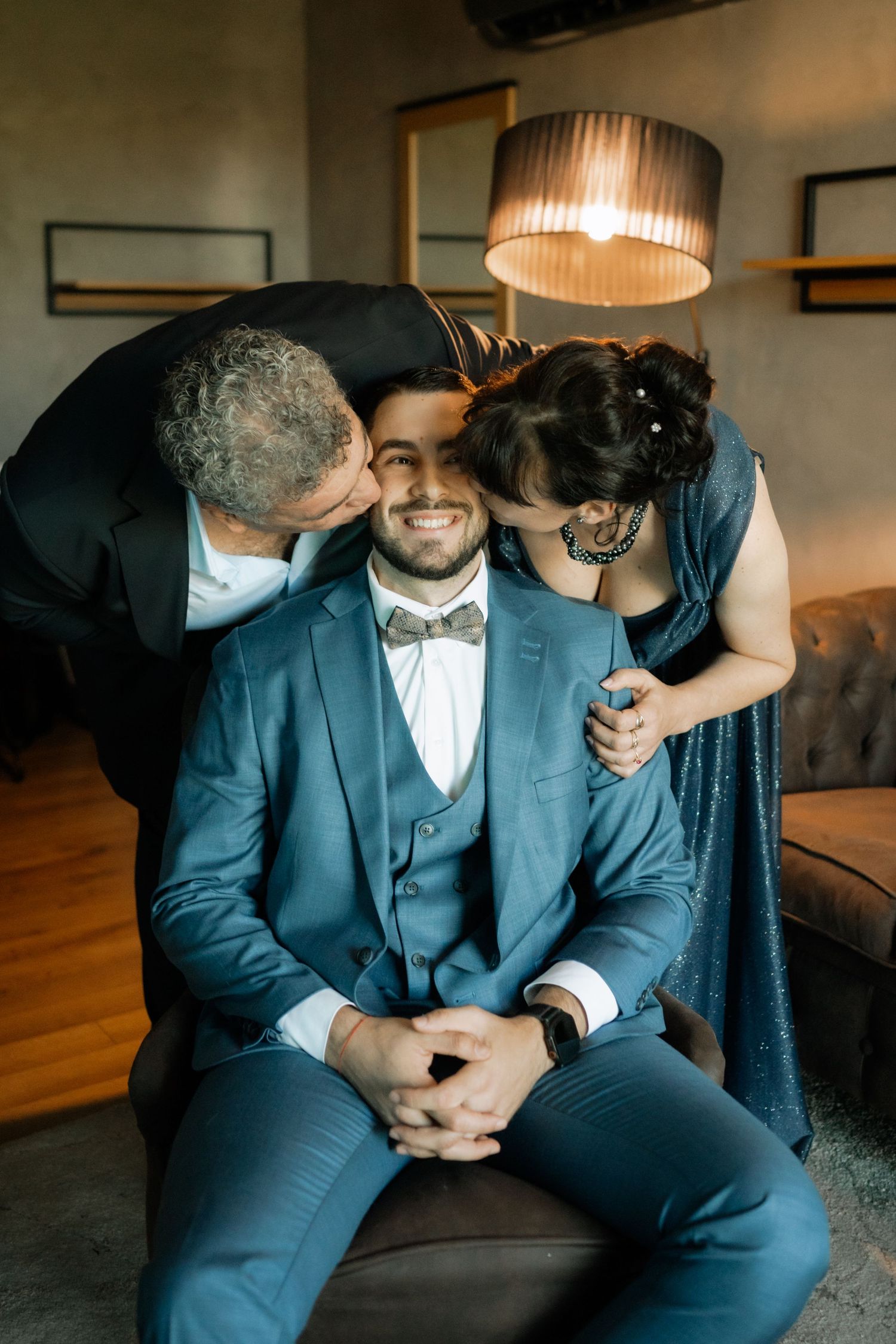 A couple in formal navy suits share intimate moments while sitting together on a couch in an indoor setting.