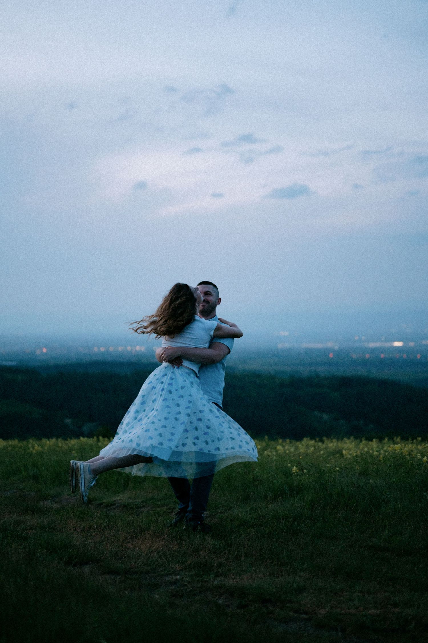 A couple performs a dramatic dance lift in a meadow against a dusky sky.