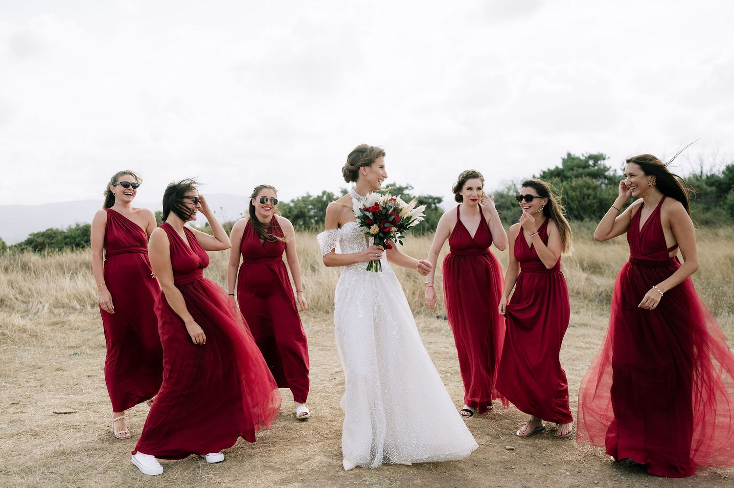 Bridal party in deep red dresses poses together on scenic outdoor terrain.