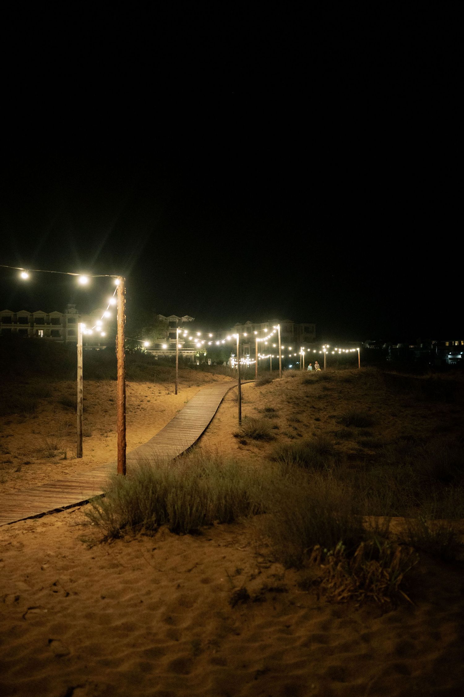 String lights illuminate a sandy beach pathway at night creating a romantic atmosphere.