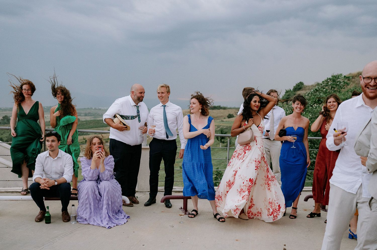 Wedding guests gather outdoors on a cloudy day for a group celebration.