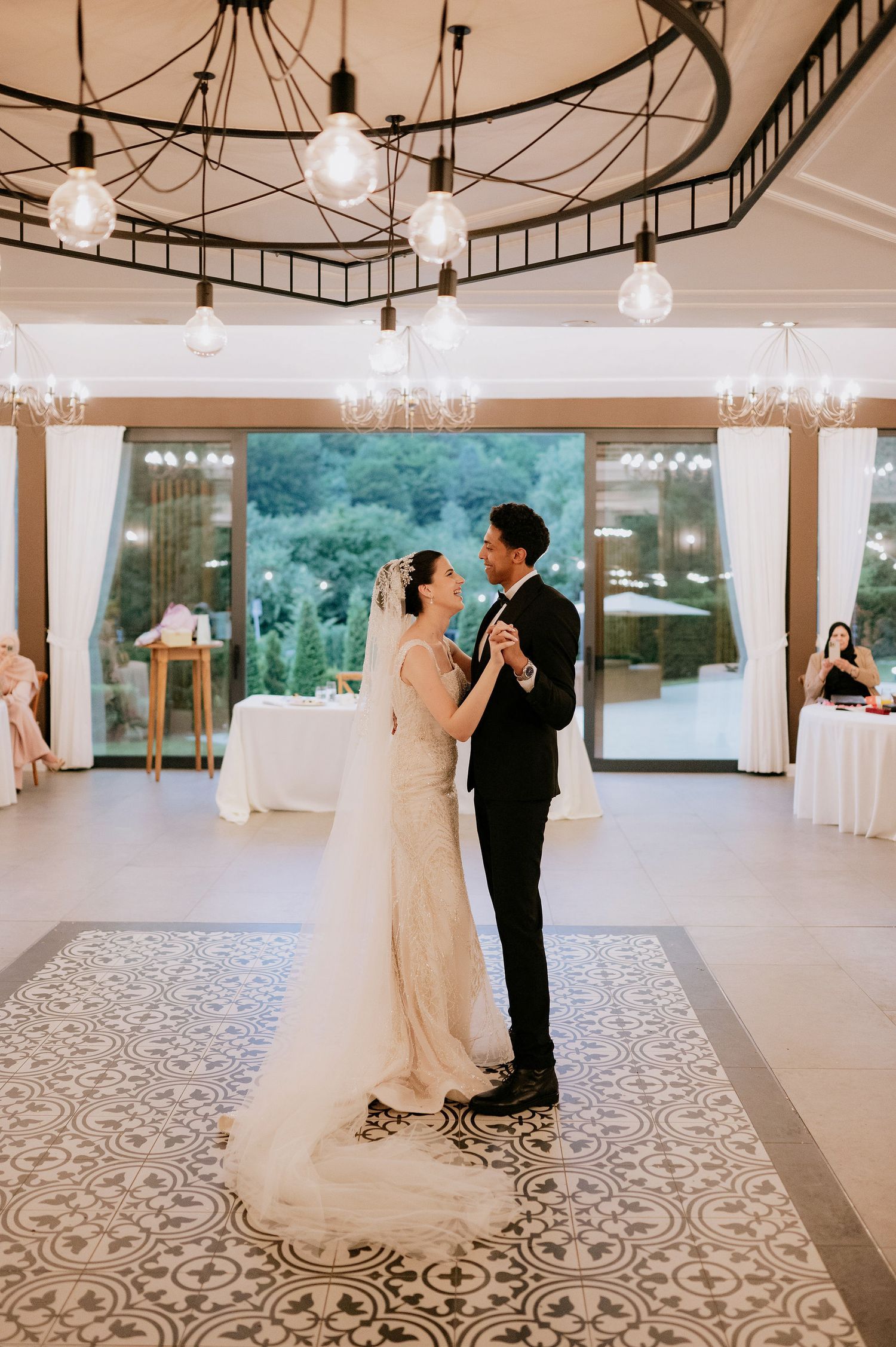 Newlyweds dance beneath industrial lighting in a modern reception venue.