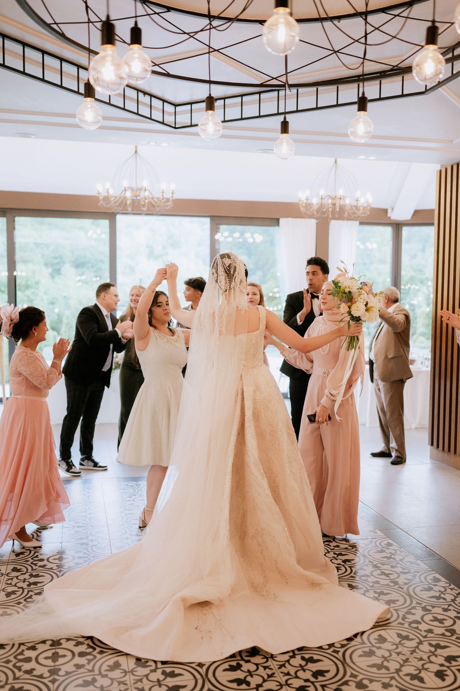 Wedding reception venue with string lights, chandeliers and guests dancing on patterned floor.