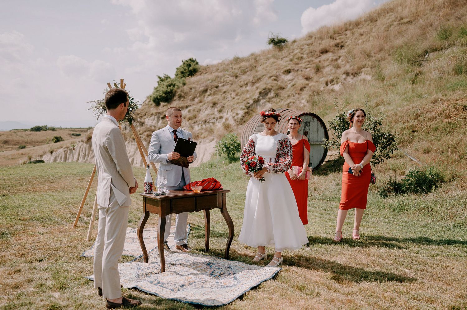 Wedding ceremony setup on a scenic hillside with guests in white and red attire.