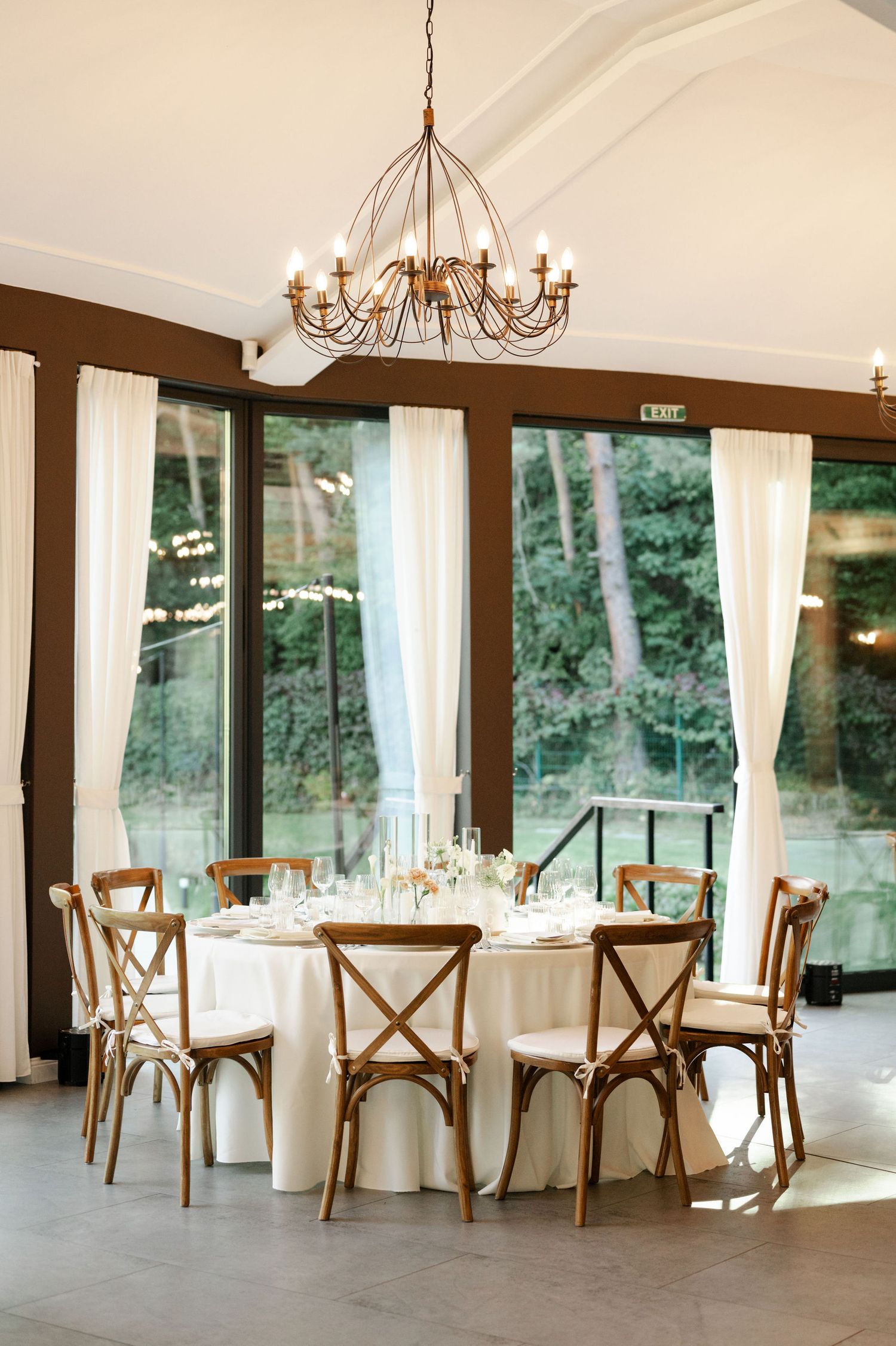 Bright banquet hall with rustic cross-back chairs and white linens set for an elegant event.
