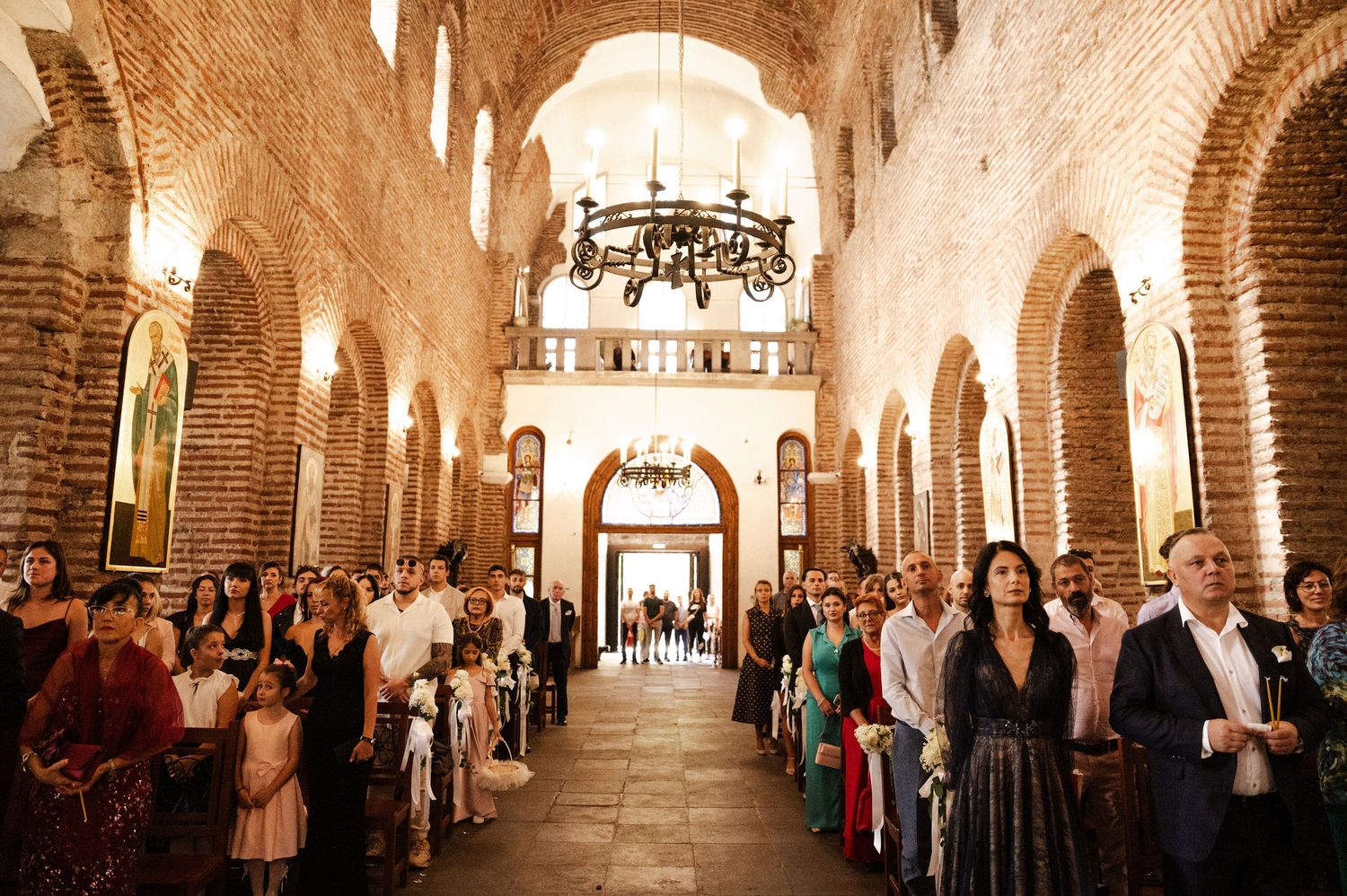 Long view of wedding ceremony in brick-lined church hall with dramatic lighting and arched architecture.