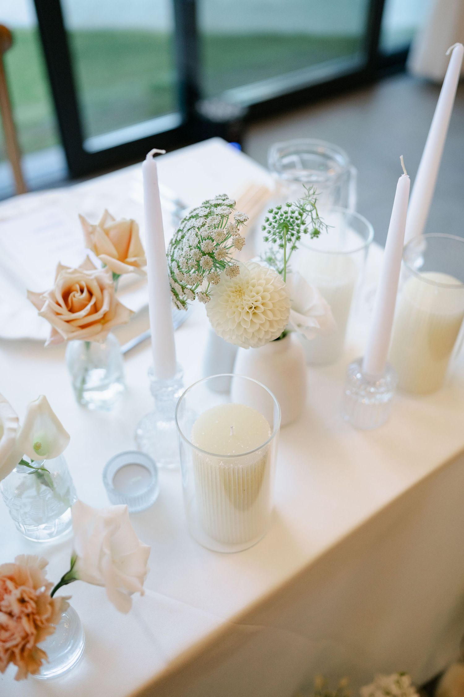 Elegant white and peach floral centerpieces with candles line a wedding reception table.