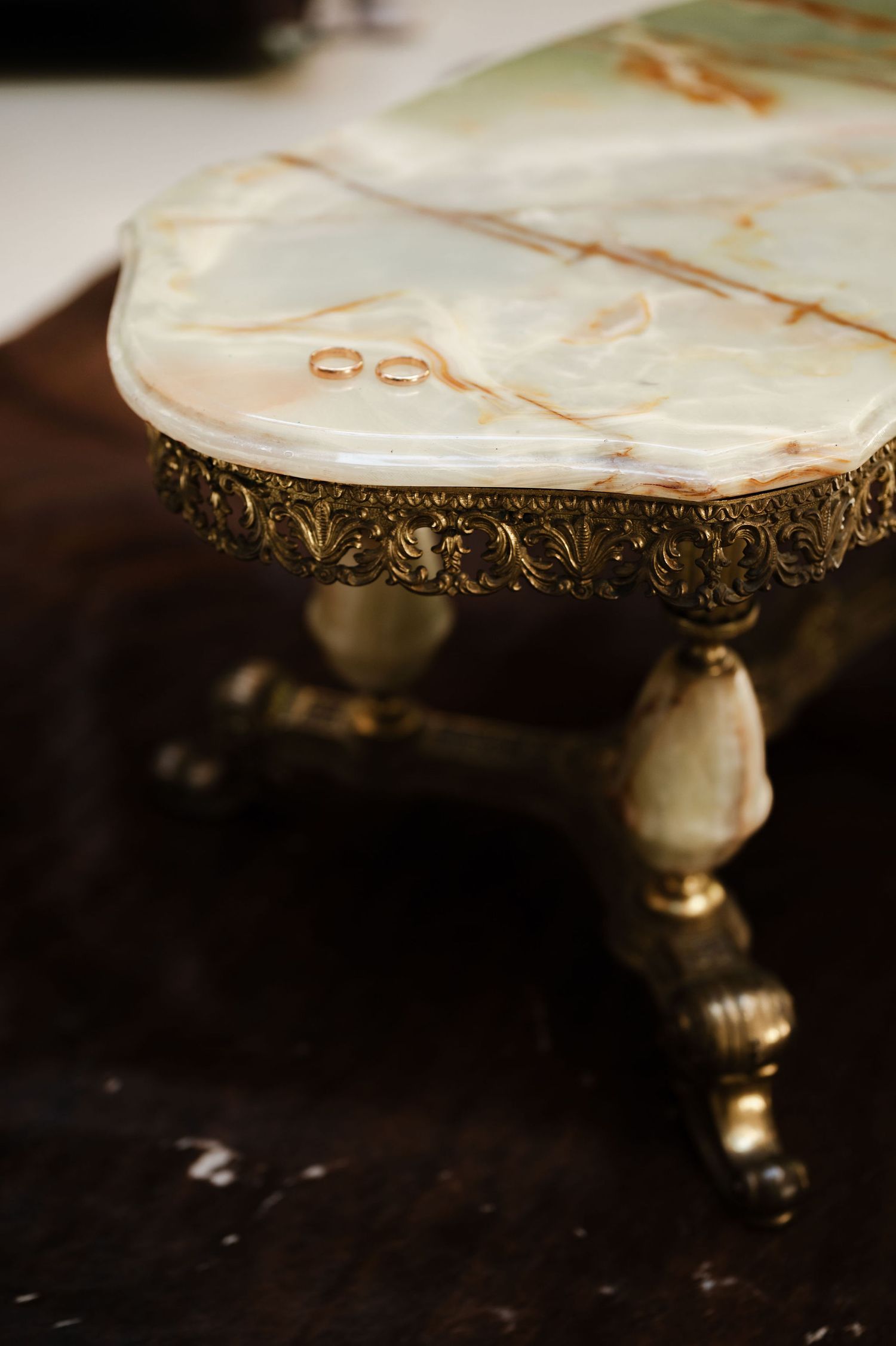 Ornate vintage marble cake stand with gold trim details photographed against dark background.