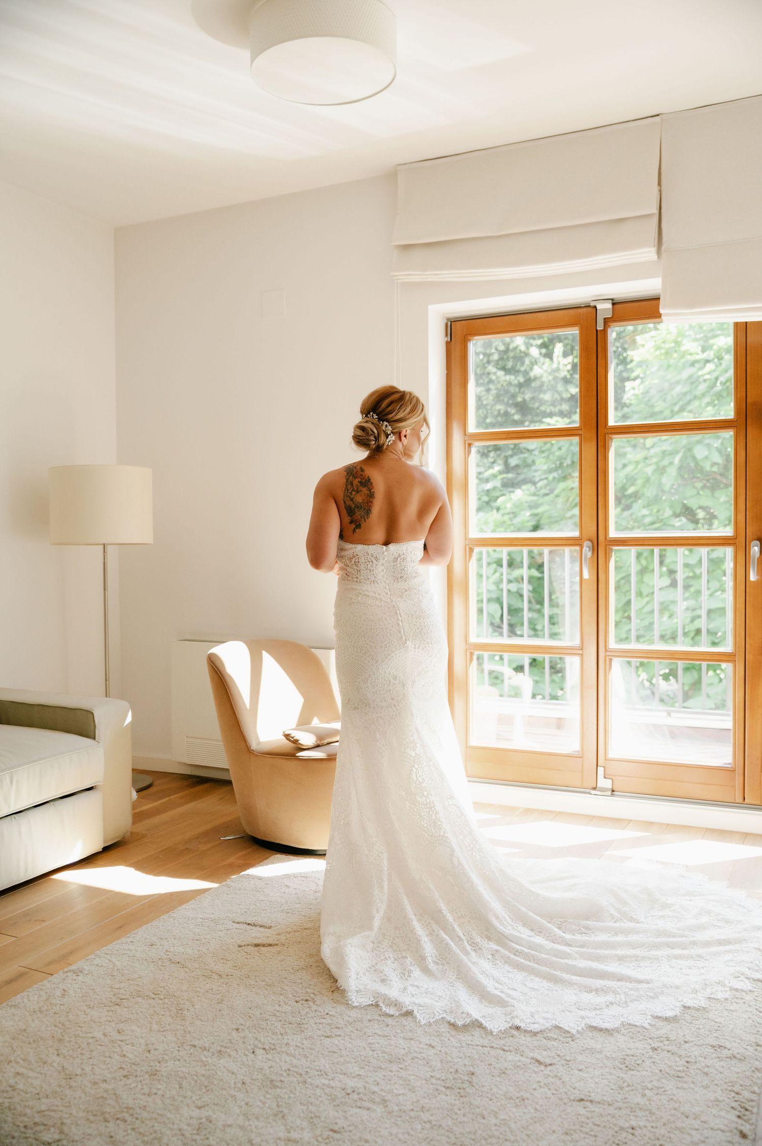 A flowing white wedding gown creates elegant shapes in a sun-filled room with wooden accents.