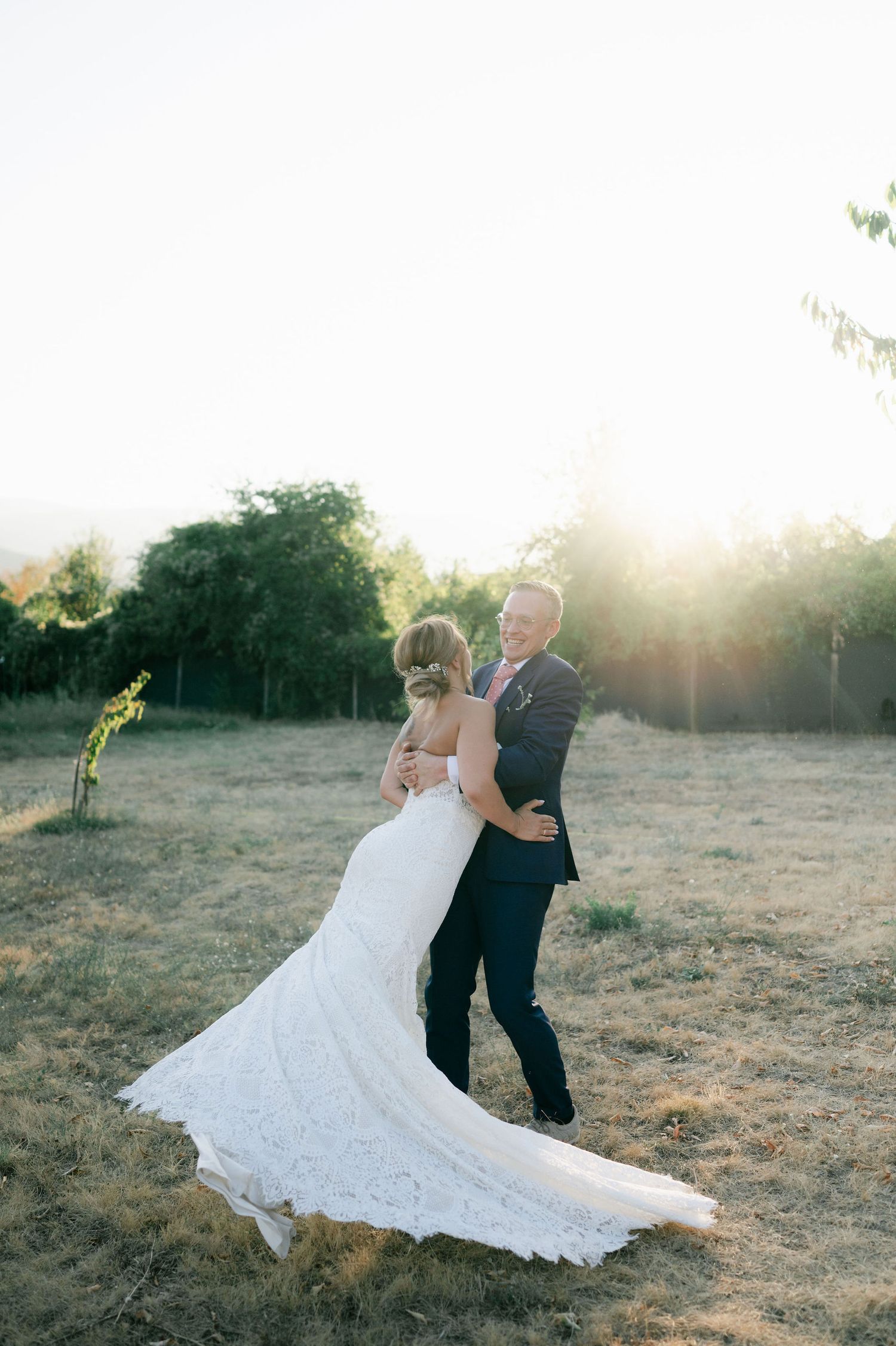 Couple performs romantic dance moves in a sunlit field during their wedding photoshoot.