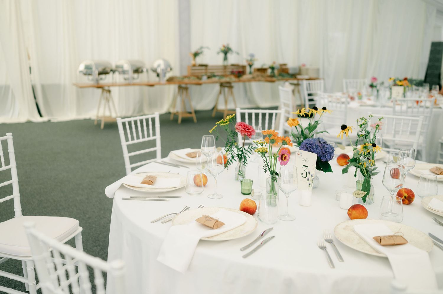 Panoramic view of a white tent wedding reception with round tables and elegant floral centerpieces.