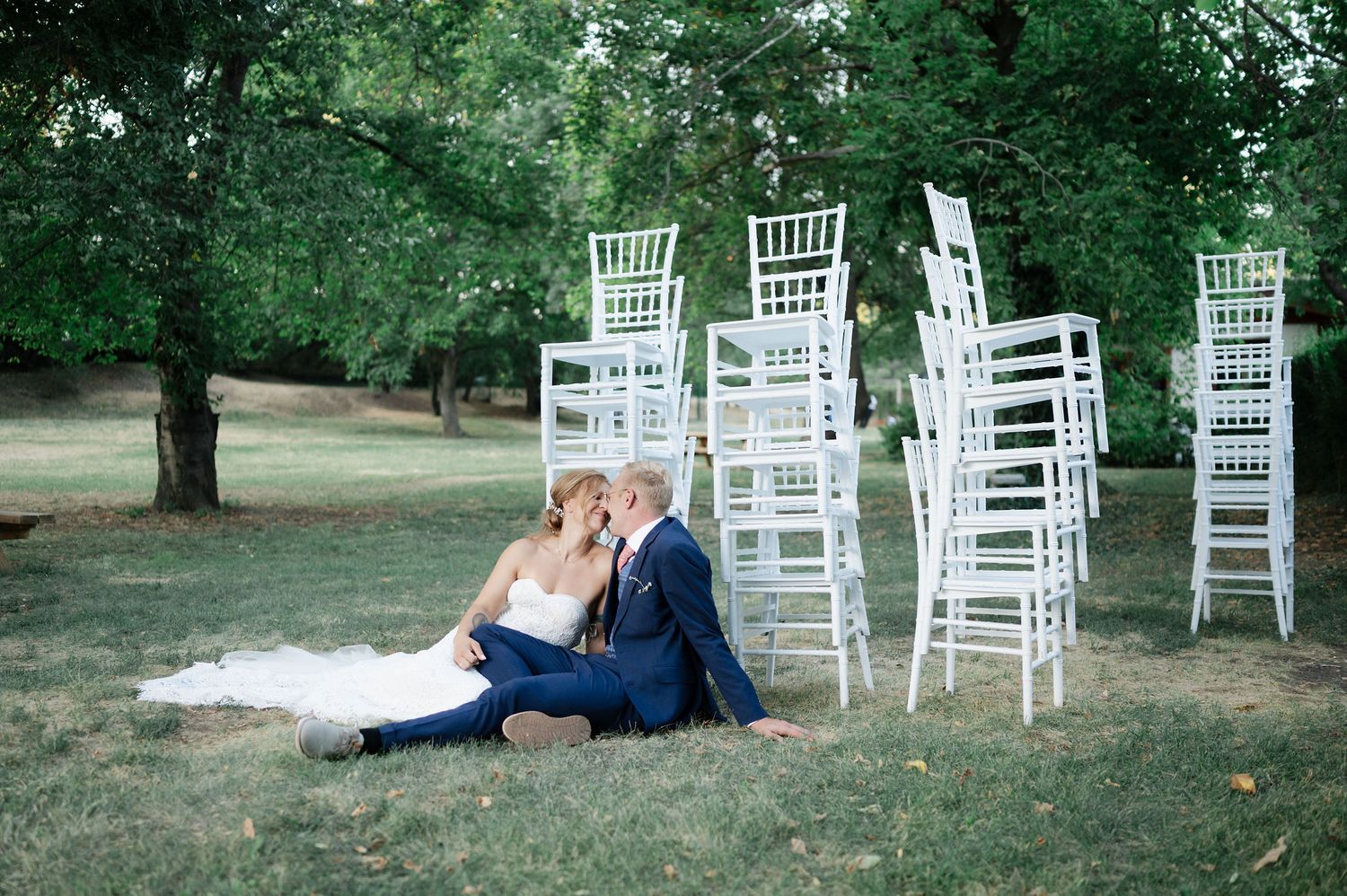 White garden chairs arranged outdoors with trees and grass creating a wedding ceremony setting.