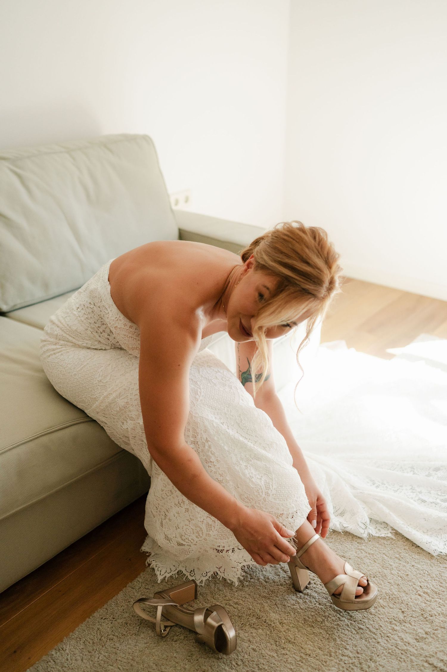 Someone in a white wedding dress bends down to fasten their sandals before the ceremony.