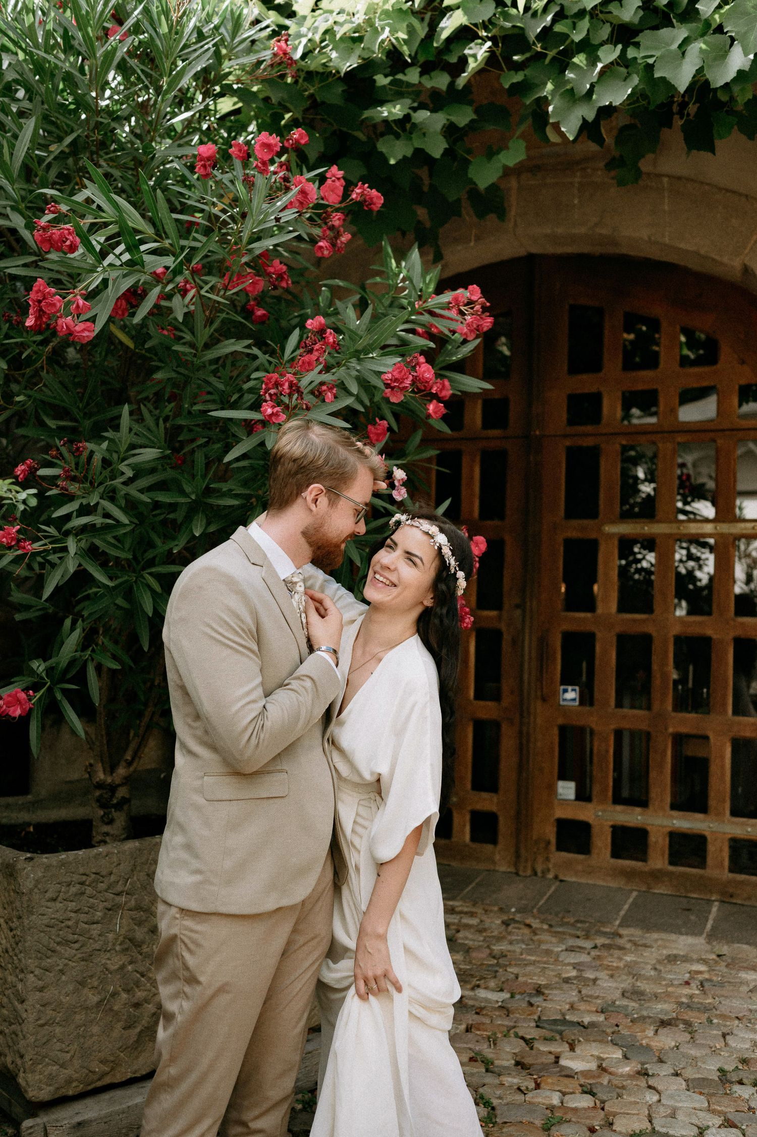 A romantic moment captured in a garden setting with red flowers and a wooden fence backdrop.