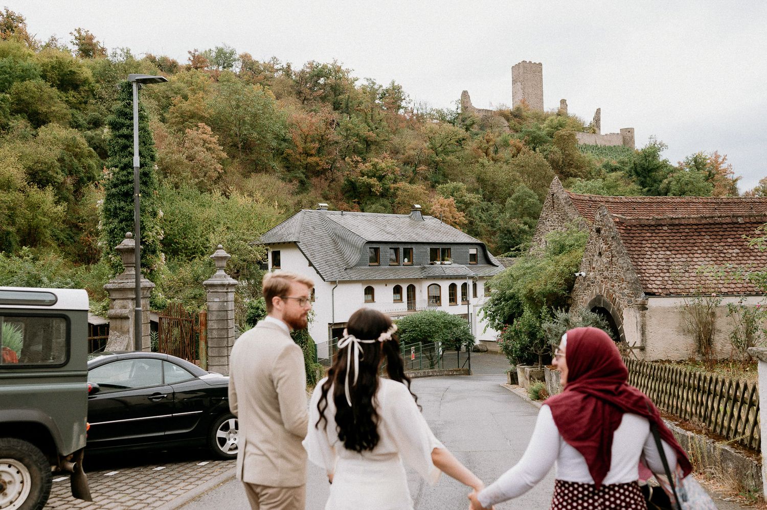 Wedding party walking along a quaint village street with historic buildings in the background.