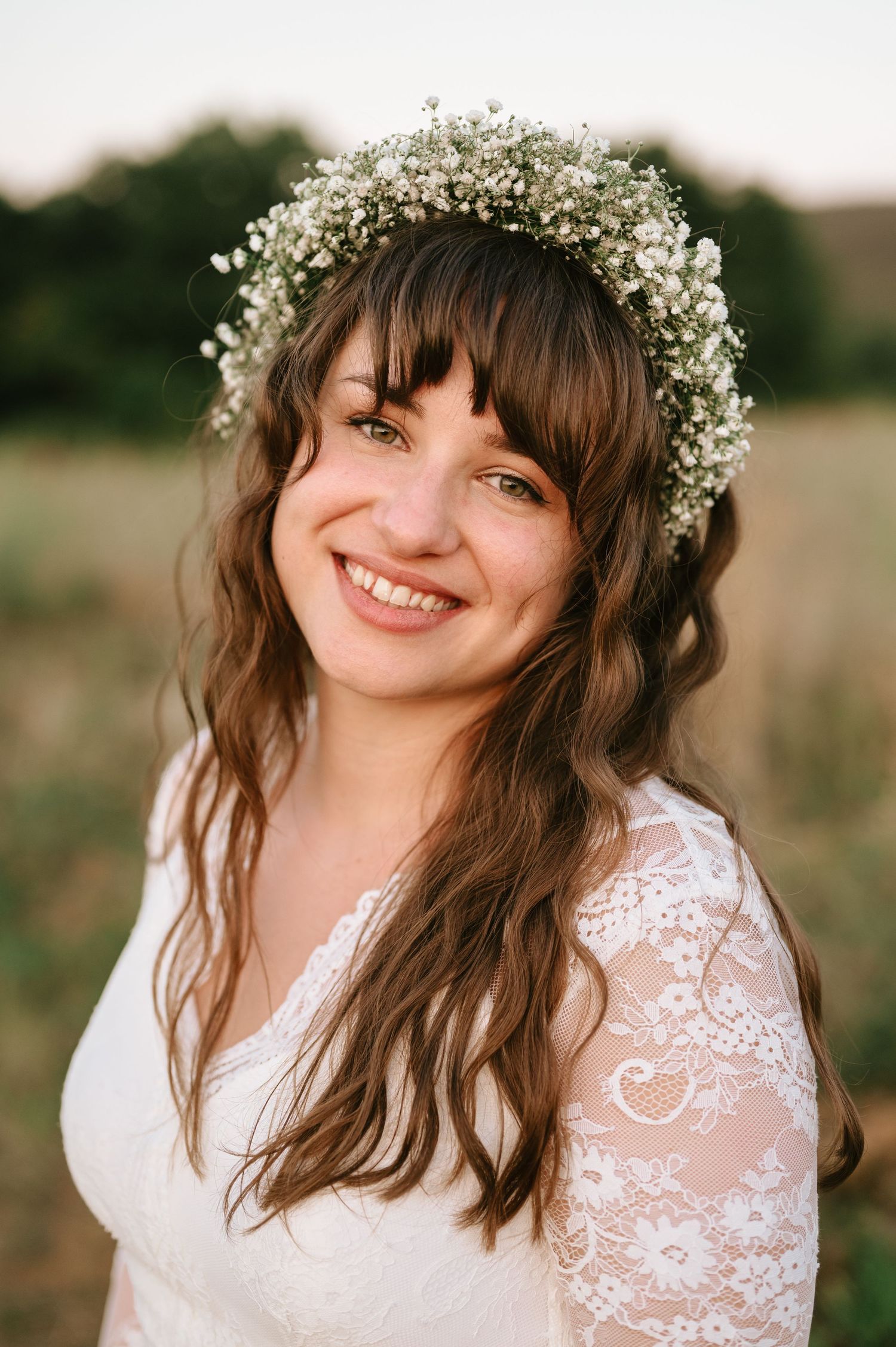 A radiant bride with baby's breath crown and lace dress smiles in golden hour light.