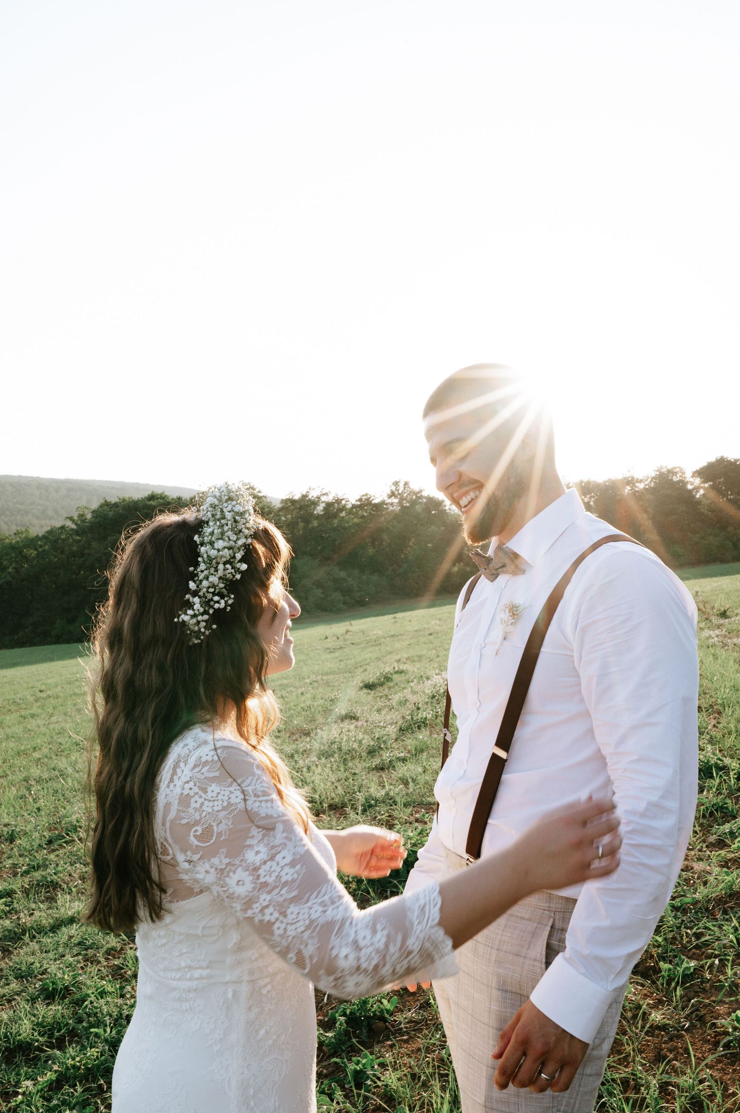 A couple in wedding attire dances playfully in a sunlit field.