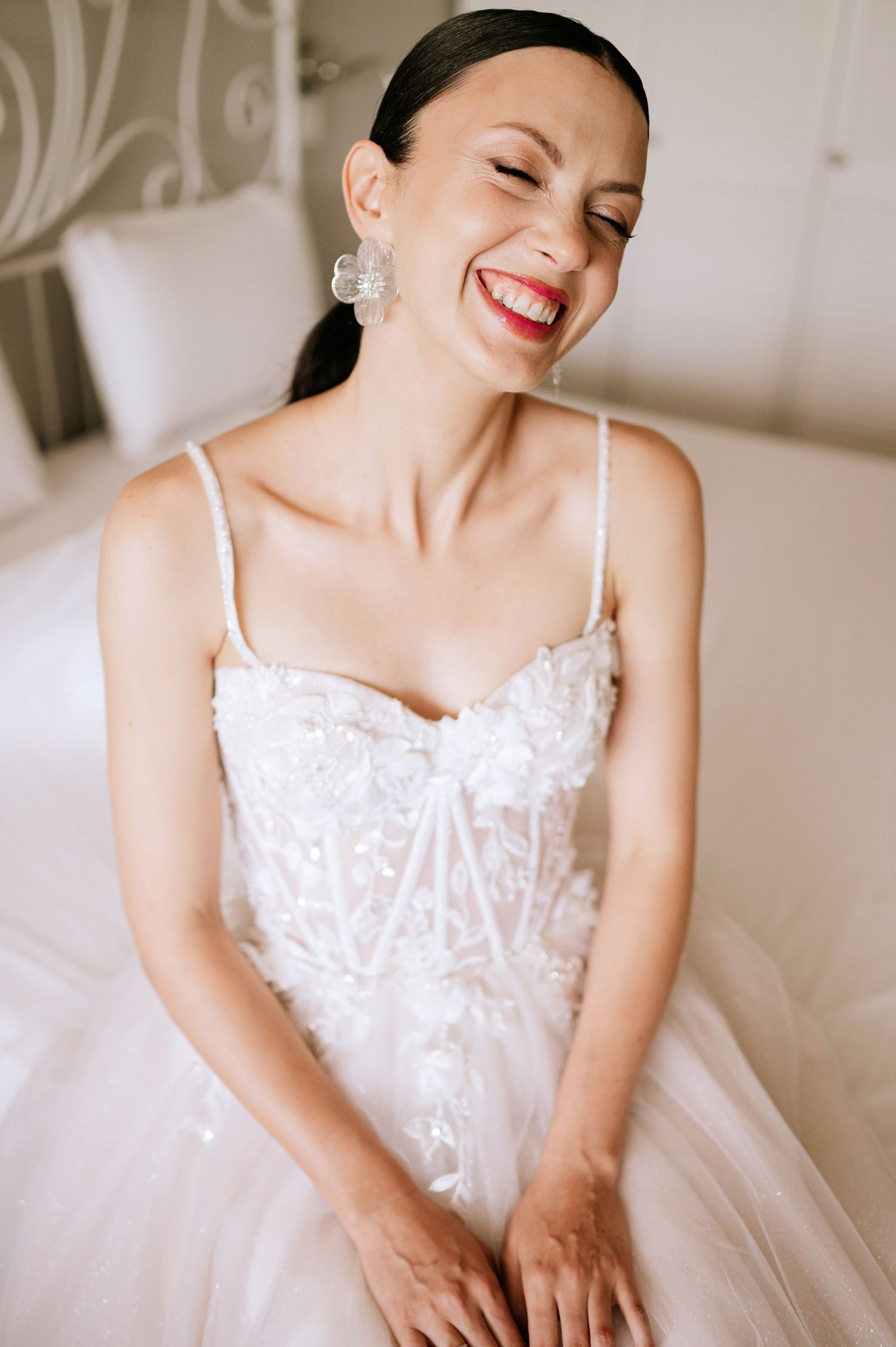 A bride in a white lace gown smiles joyfully while getting ready on her wedding day.