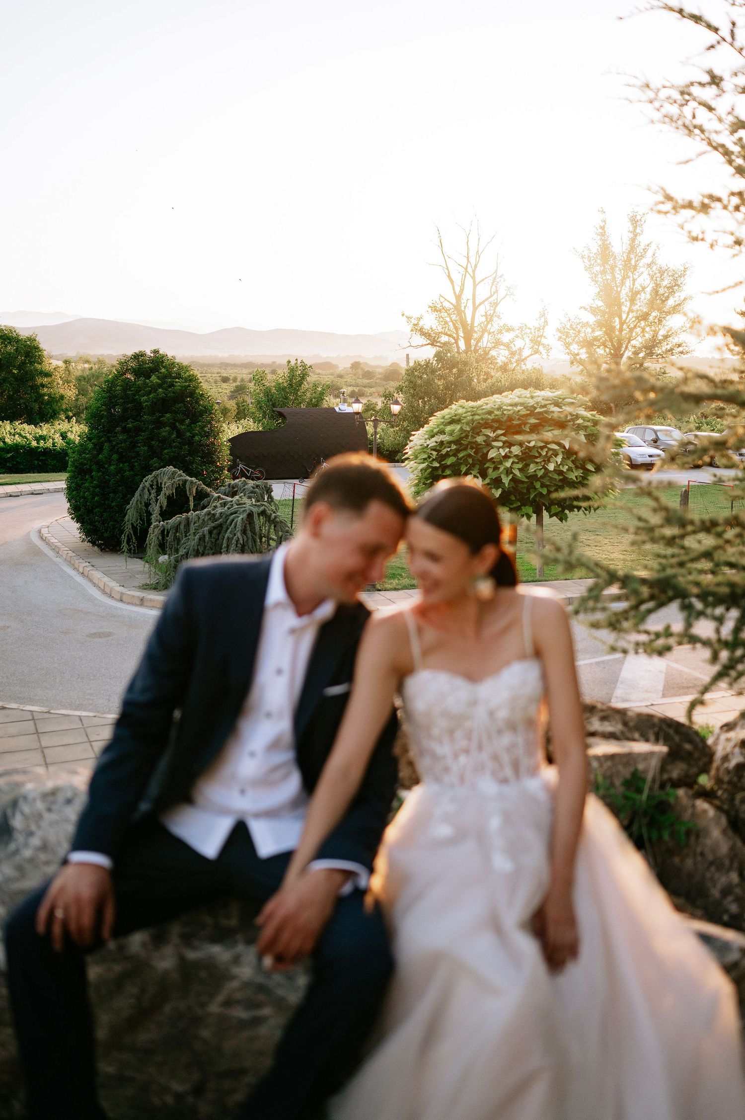 Wedding couple sitting close together on natural stone during golden hour.