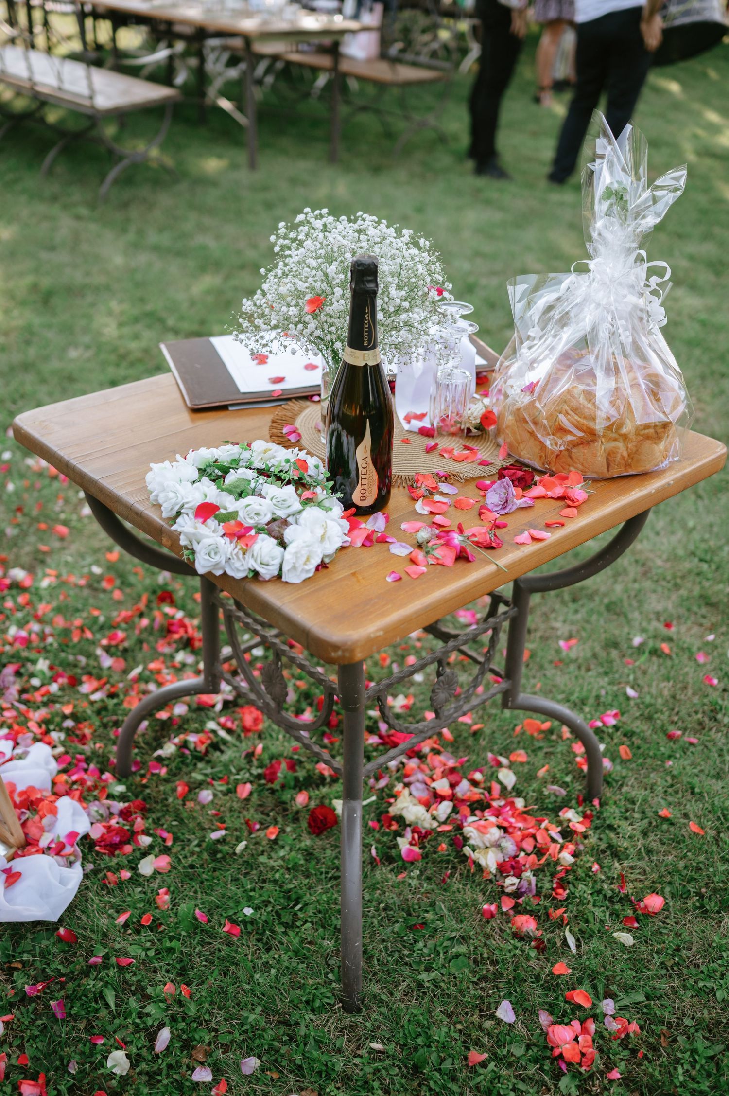 Wooden table decorated with wrapped favors and rose petals for an outdoor wedding celebration.